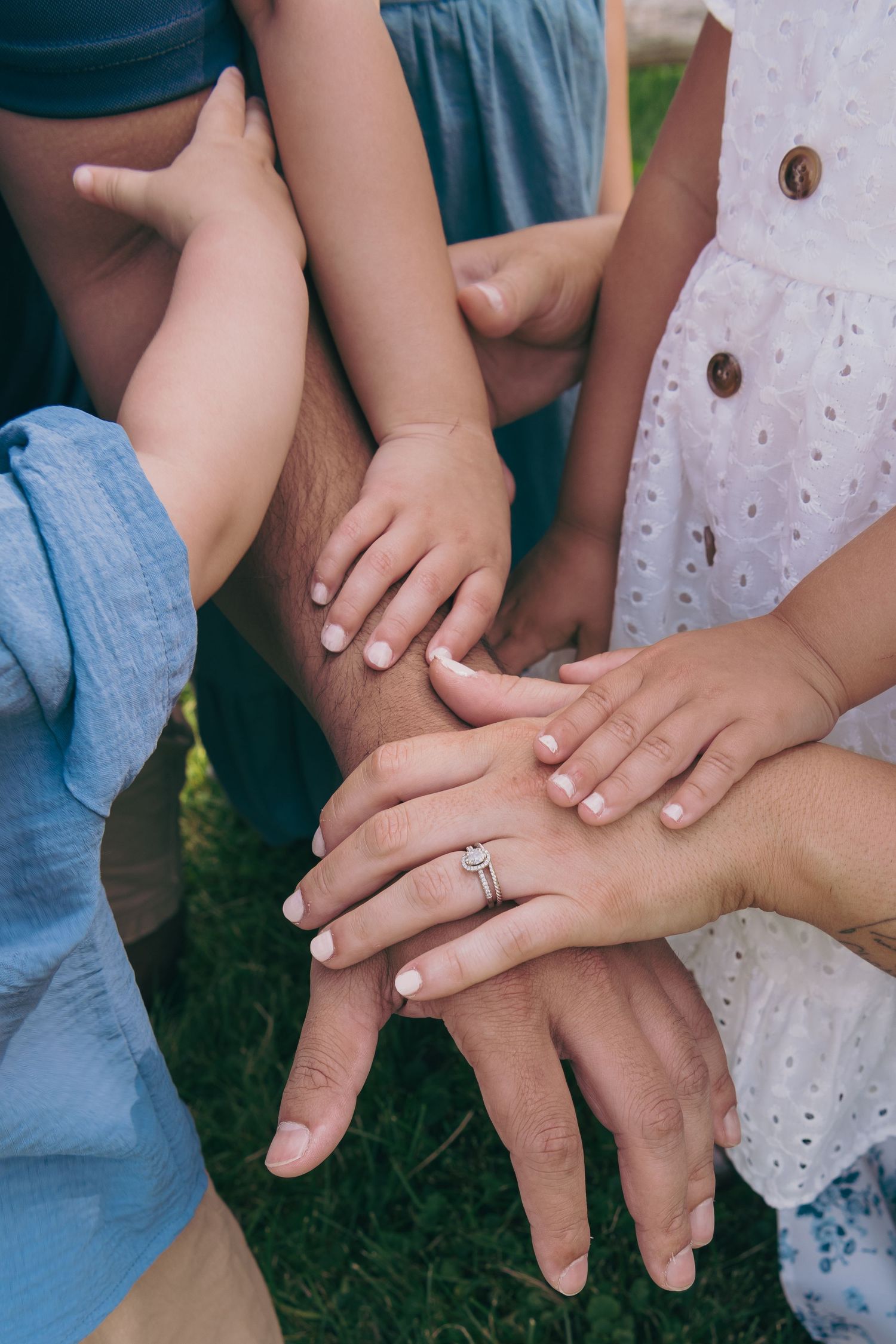 Multiple hands stacked together showing unity and connection, with one hand wearing an engagement ring.