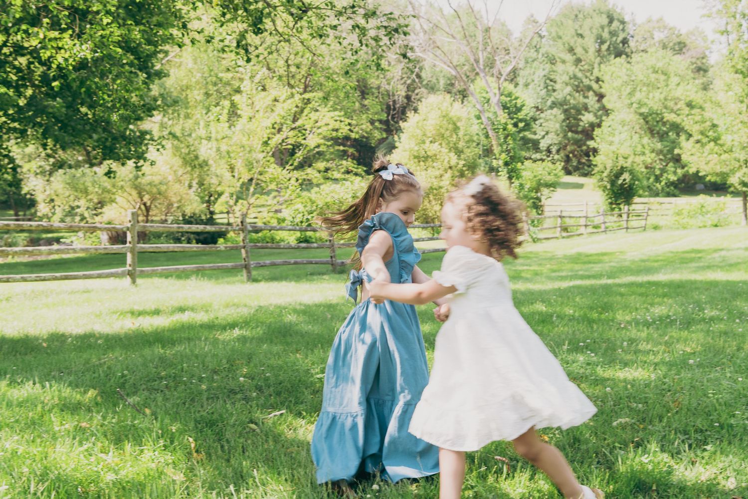 Two children twirling and dancing together in white and blue dresses on a sunny lawn.