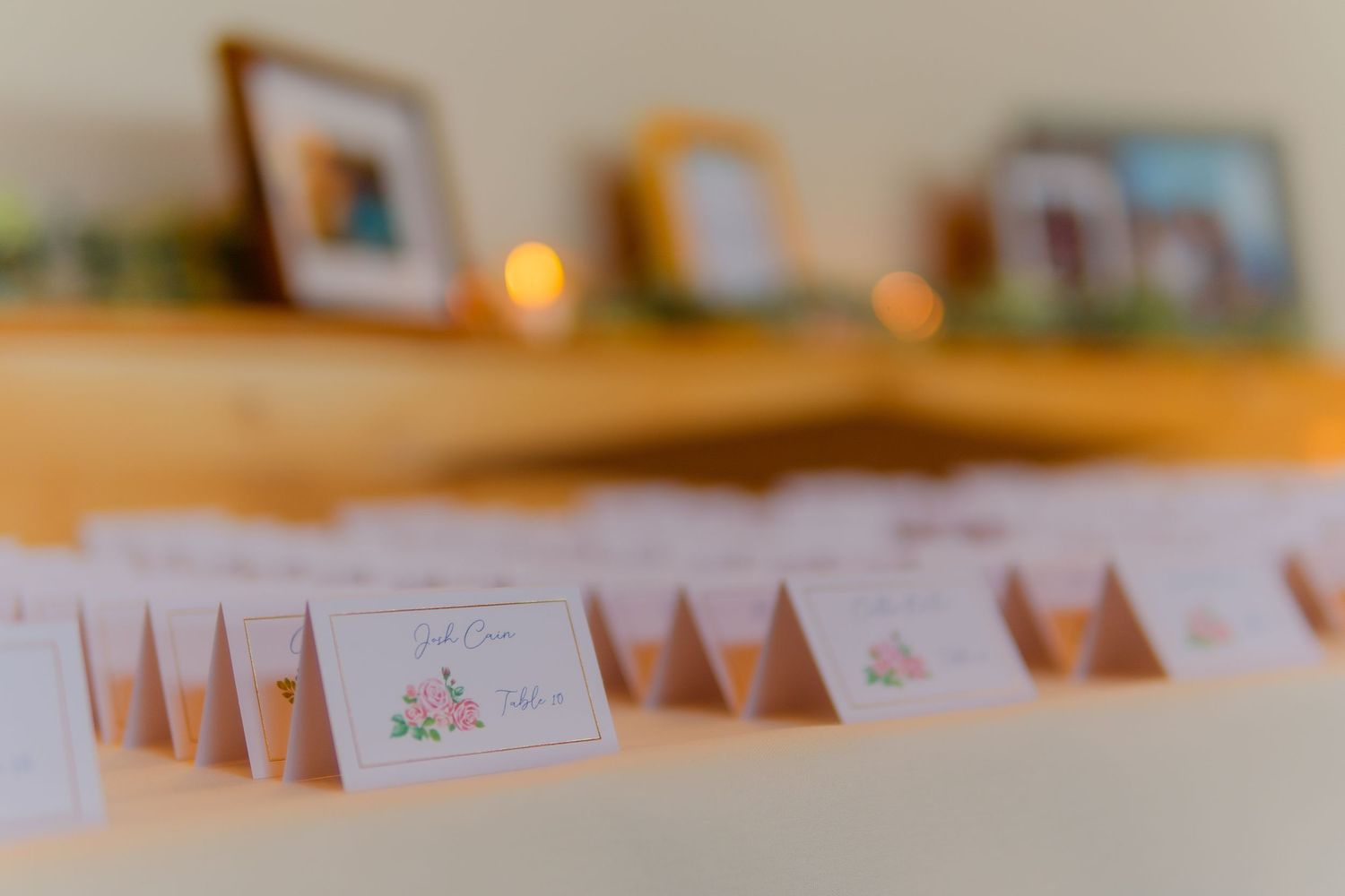 Wedding place cards with handwritten names displayed on wooden tables with warm lighting and soft focus detail.