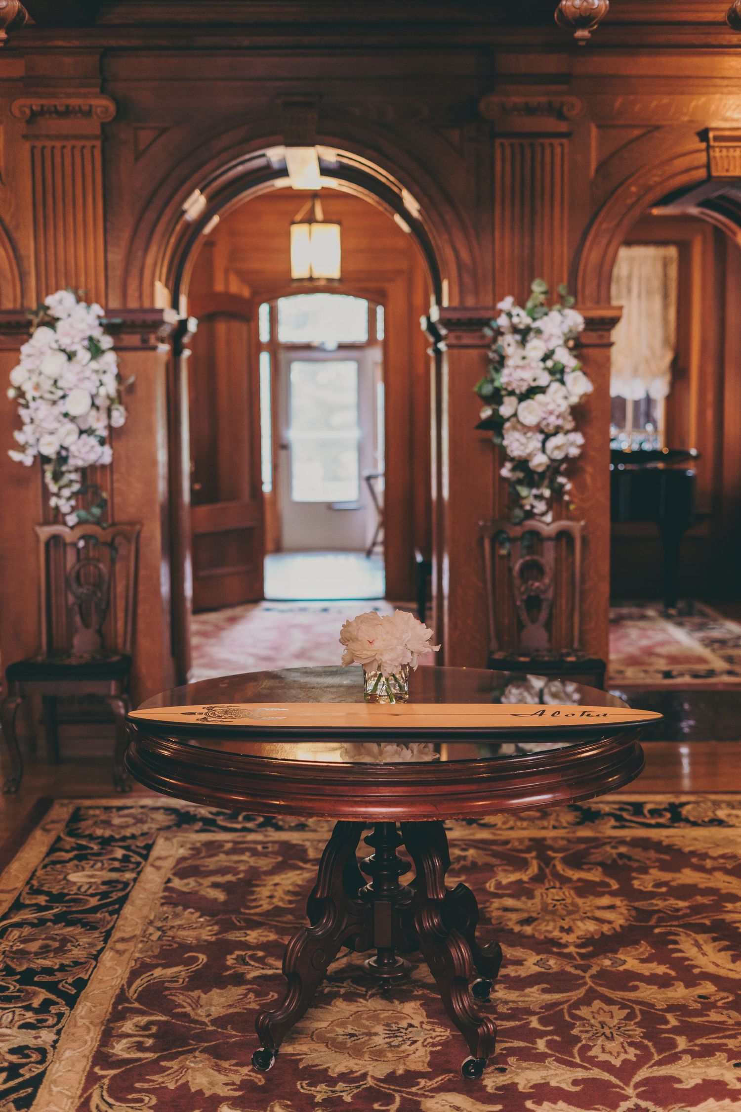 Elegant wooden tables with floral centerpieces set in a grand Victorian ballroom with ornate carpeting and carved details.