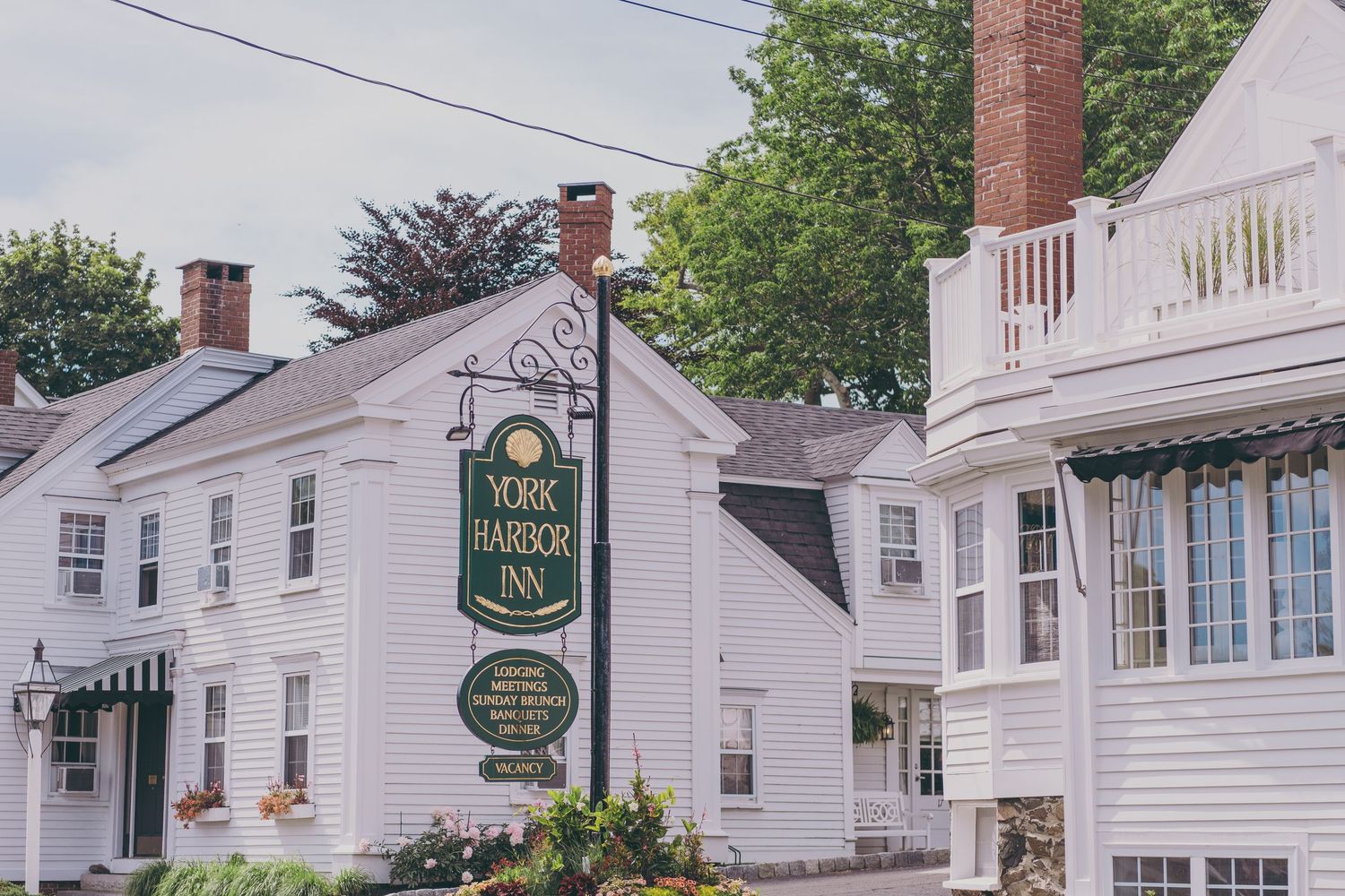 A quaint white colonial inn with green sign and red brick chimneys stands along a New England street.