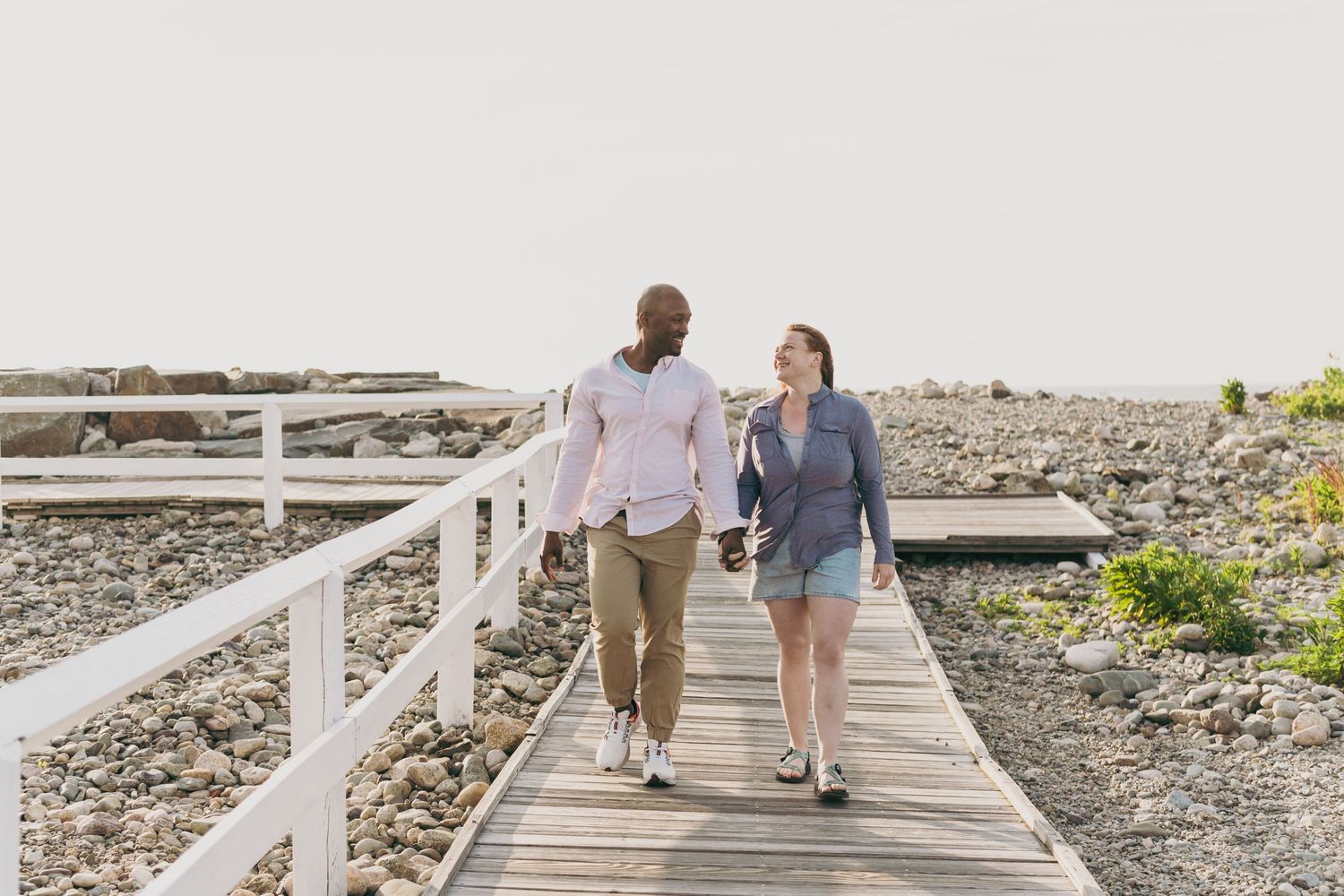 Two people enjoying a casual stroll together on a wooden boardwalk along a scenic coastal shoreline.