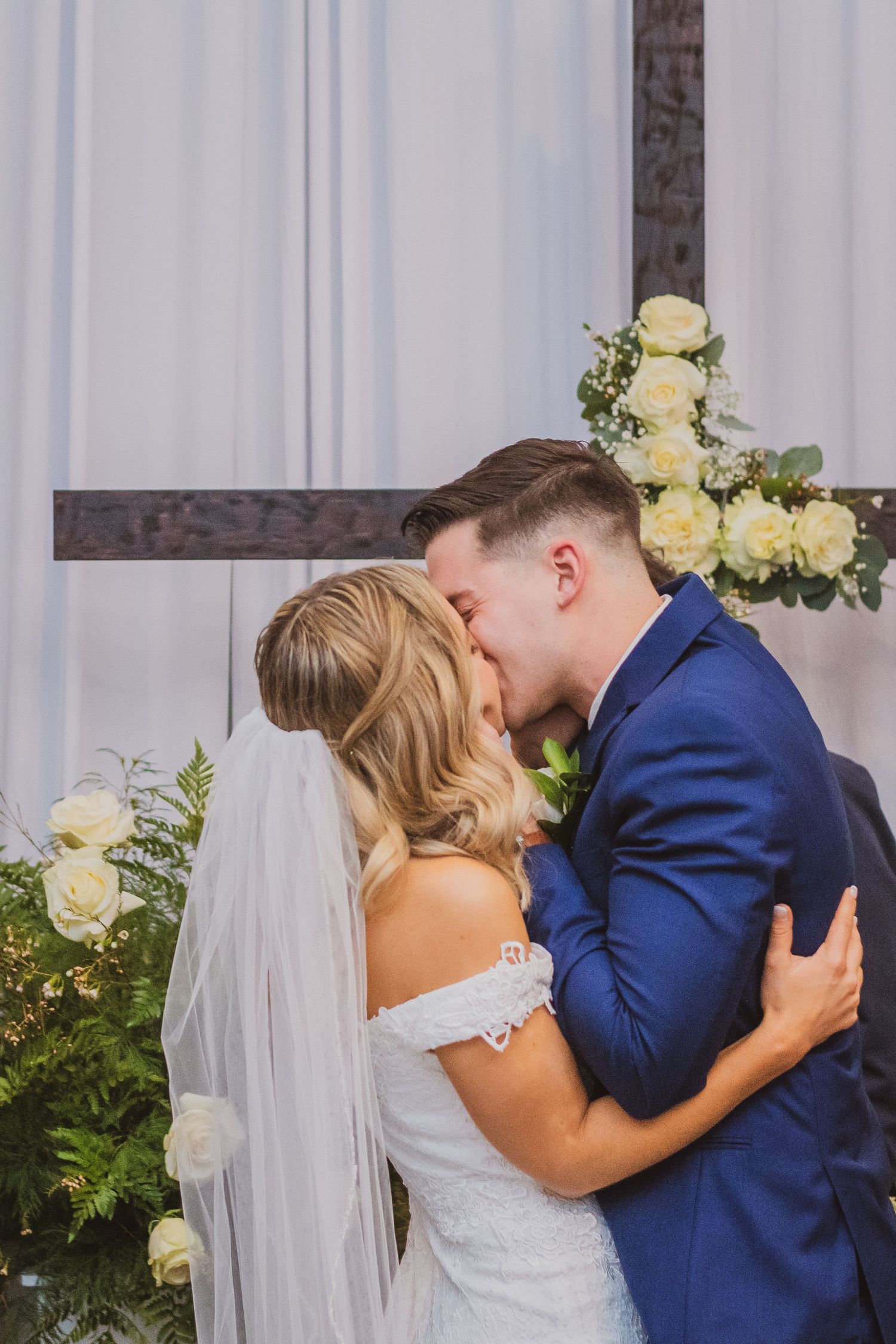 A sequence of four wedding photos shows a romantic kiss between newlyweds in front of white curtains and cream roses.
