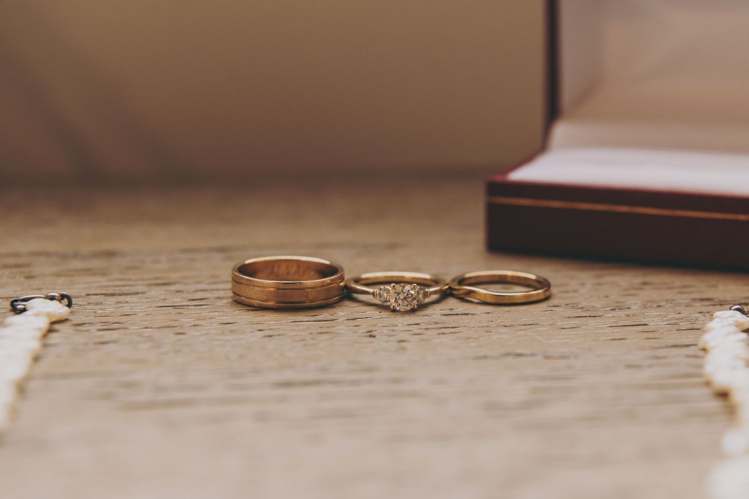 Three wedding rings arranged on a rustic textured surface, including two gold bands and one diamond engagement ring.
