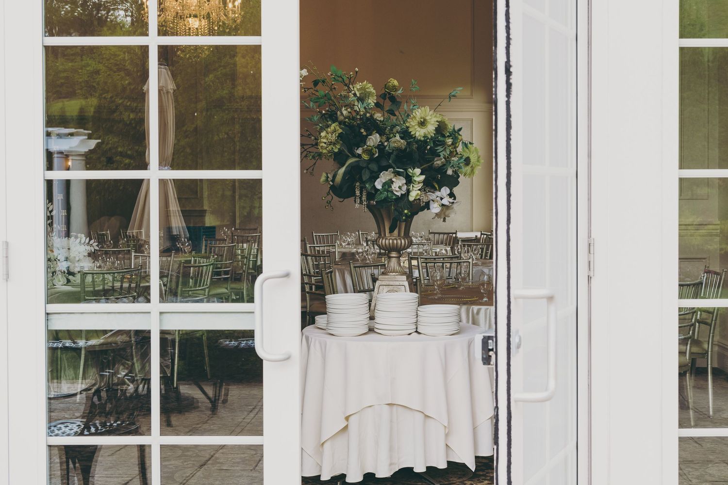White French doors open to reveal an elegant restaurant interior with a floral centerpiece on a white tablecloth.