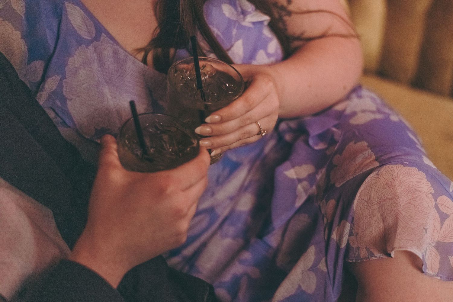 Close up detail shot of hands holding a camera against purple floral fabric.