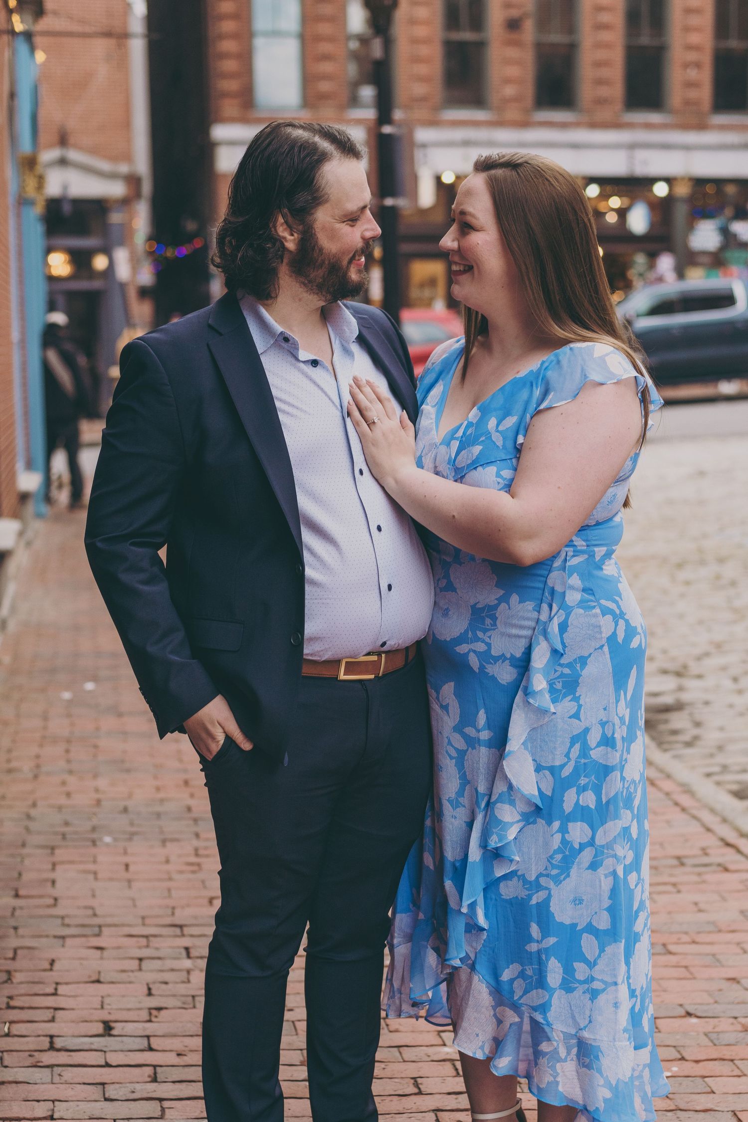 A couple sharing a joyful moment on a brick sidewalk in urban setting.