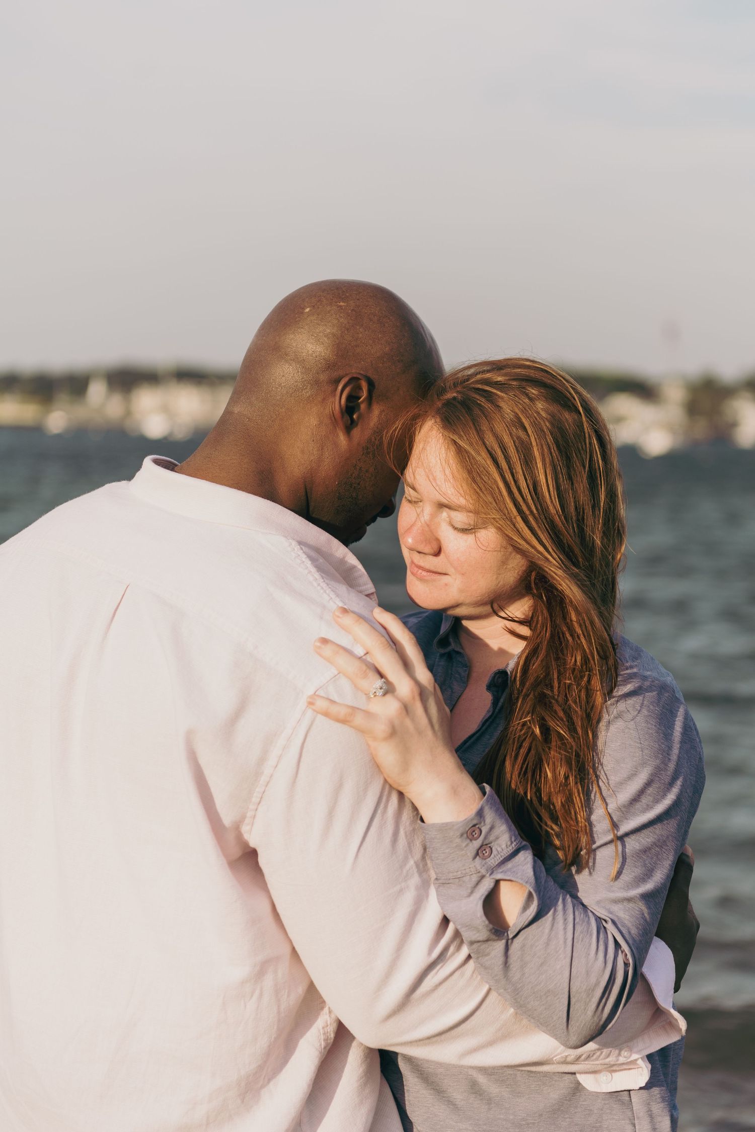 A romantic couple embraces tenderly by the waterfront during golden hour.