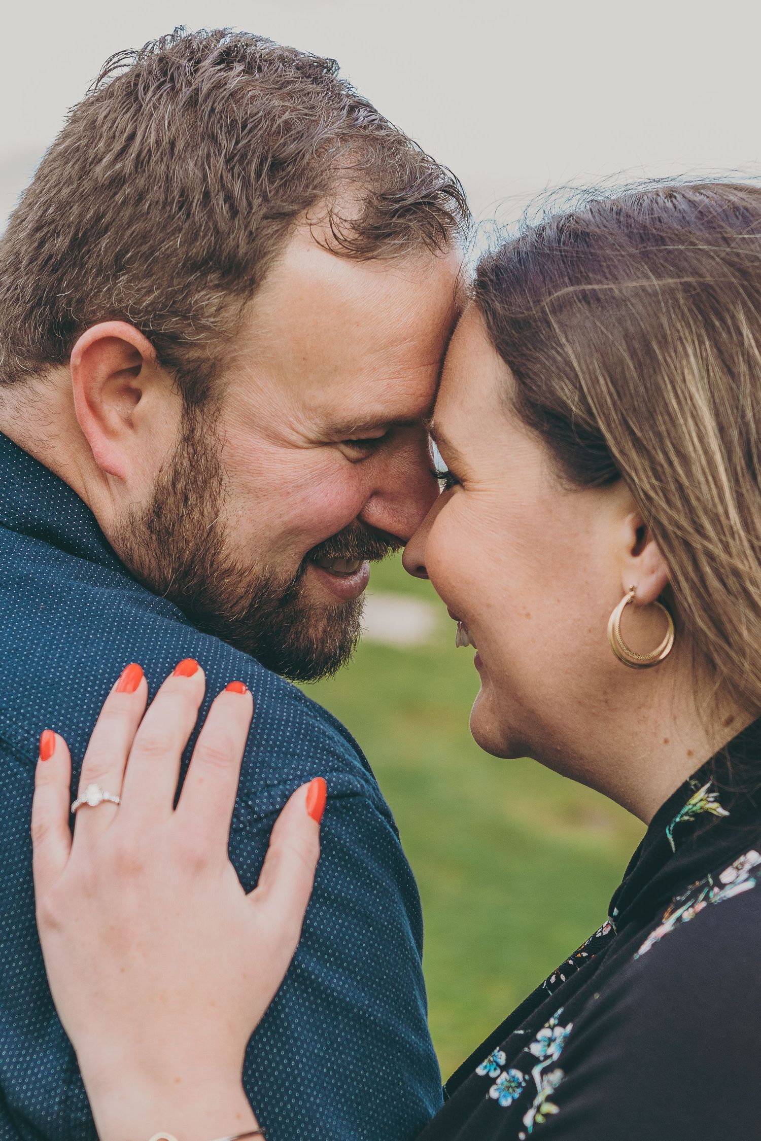 Close-up intimate moment between a couple sharing a tender smile while wearing casual attire outdoors.