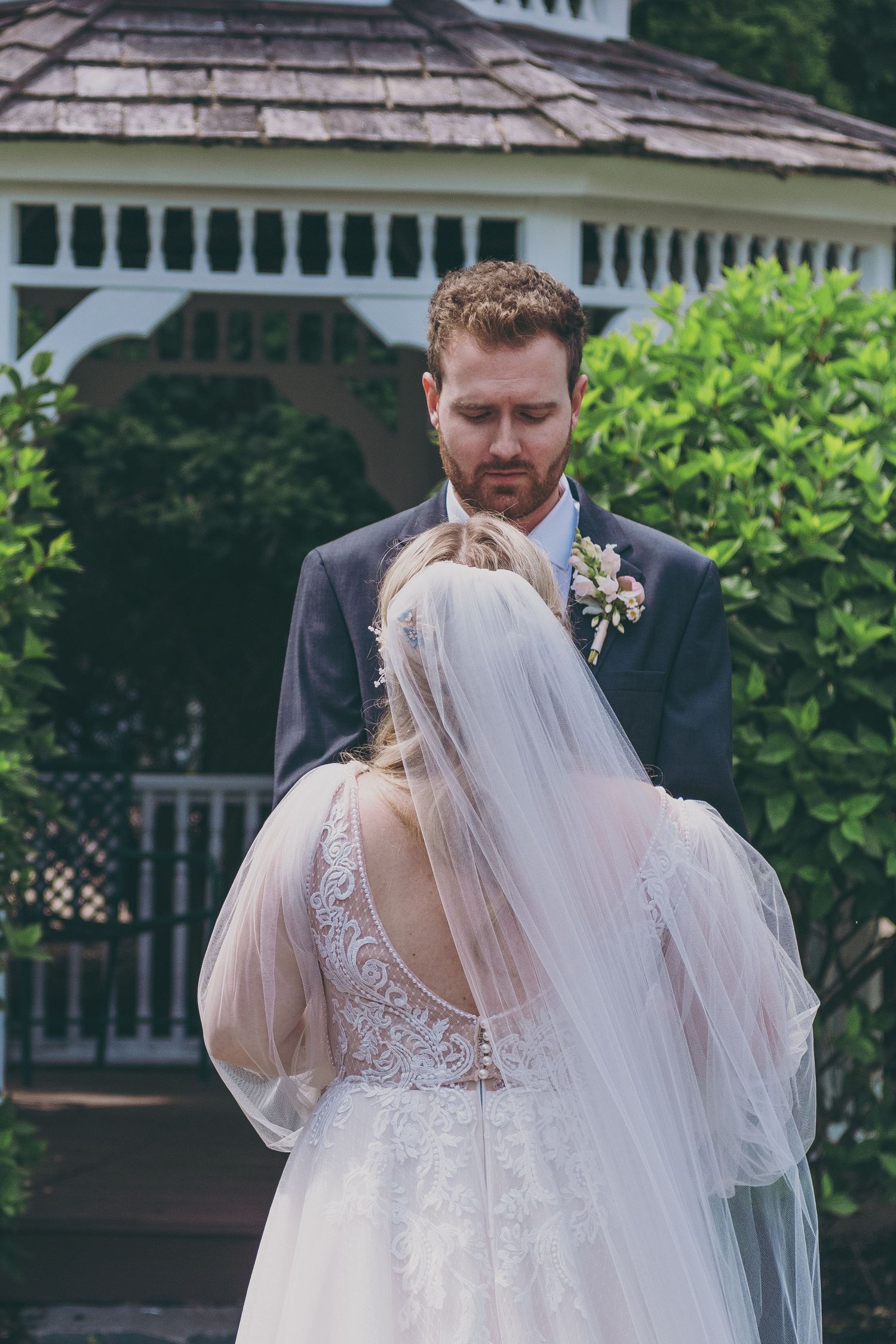 Bride and groom share intimate moment in front of white garden gazebo during outdoor wedding ceremony.