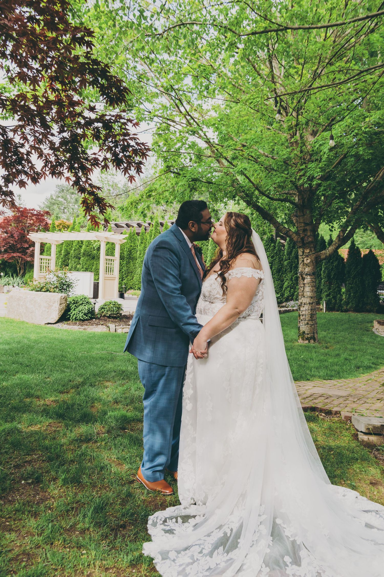 A romantic garden wedding photoshoot captures five tender moments between a couple among lush green trees and foliage.