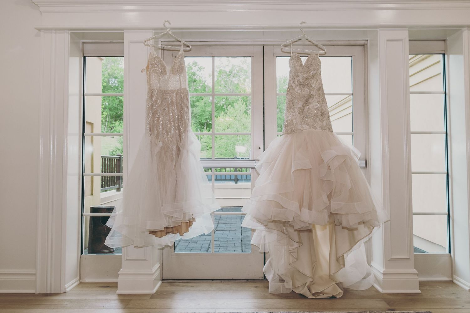 A row of elegant white wedding dresses displayed on hangers in a bridal boutique with natural light streaming through windows.