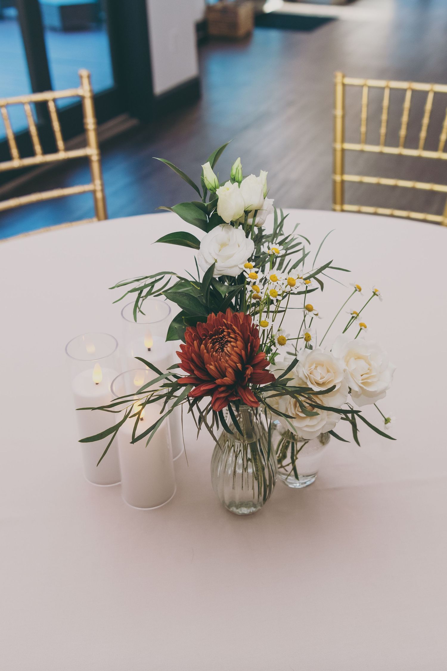 Elegant floral centerpiece with burgundy and white blooms on round table with gold chiavari chairs.
