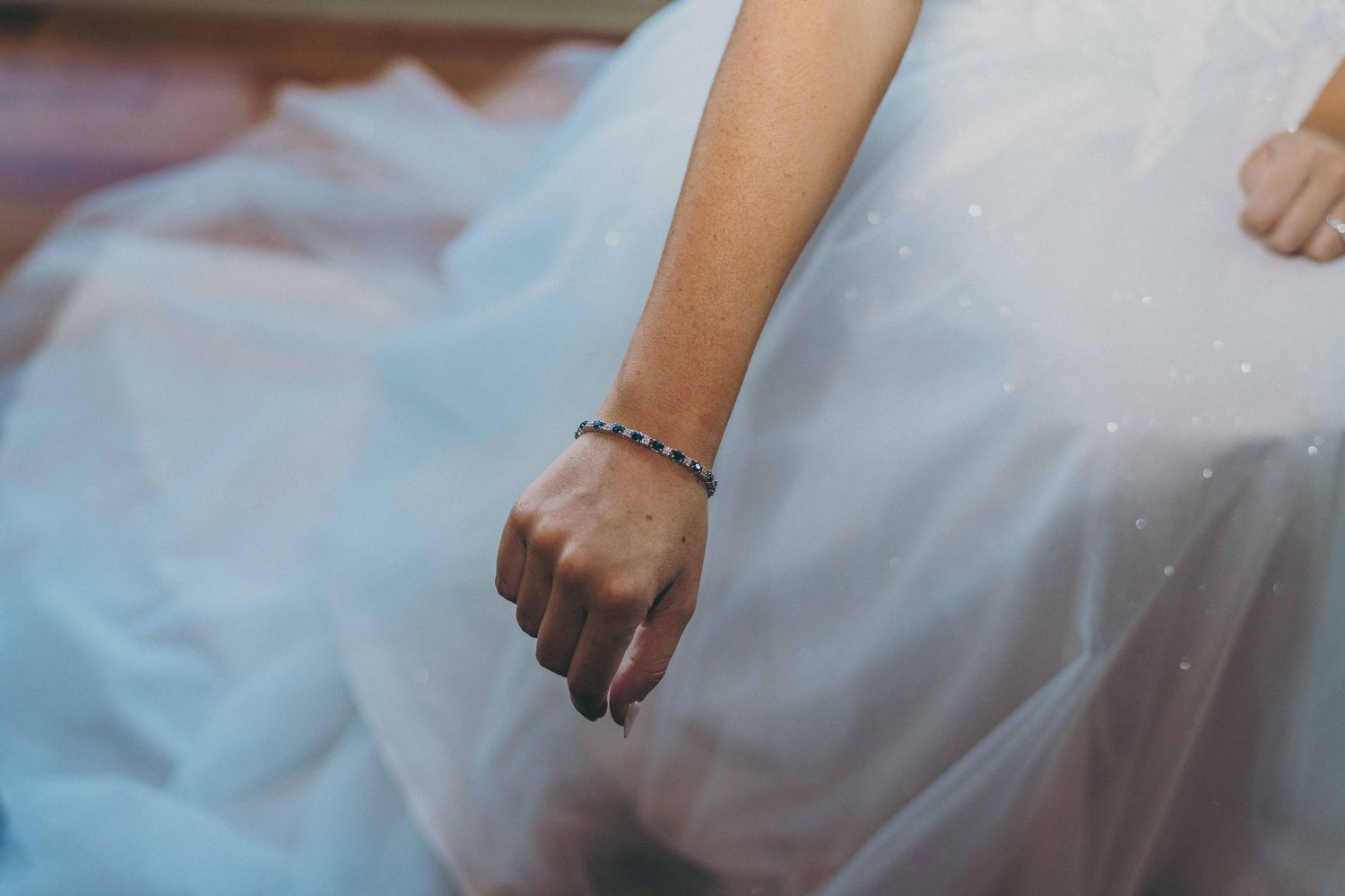 A delicate bracelet adorns a hand resting against flowing white tulle fabric of a wedding dress.
