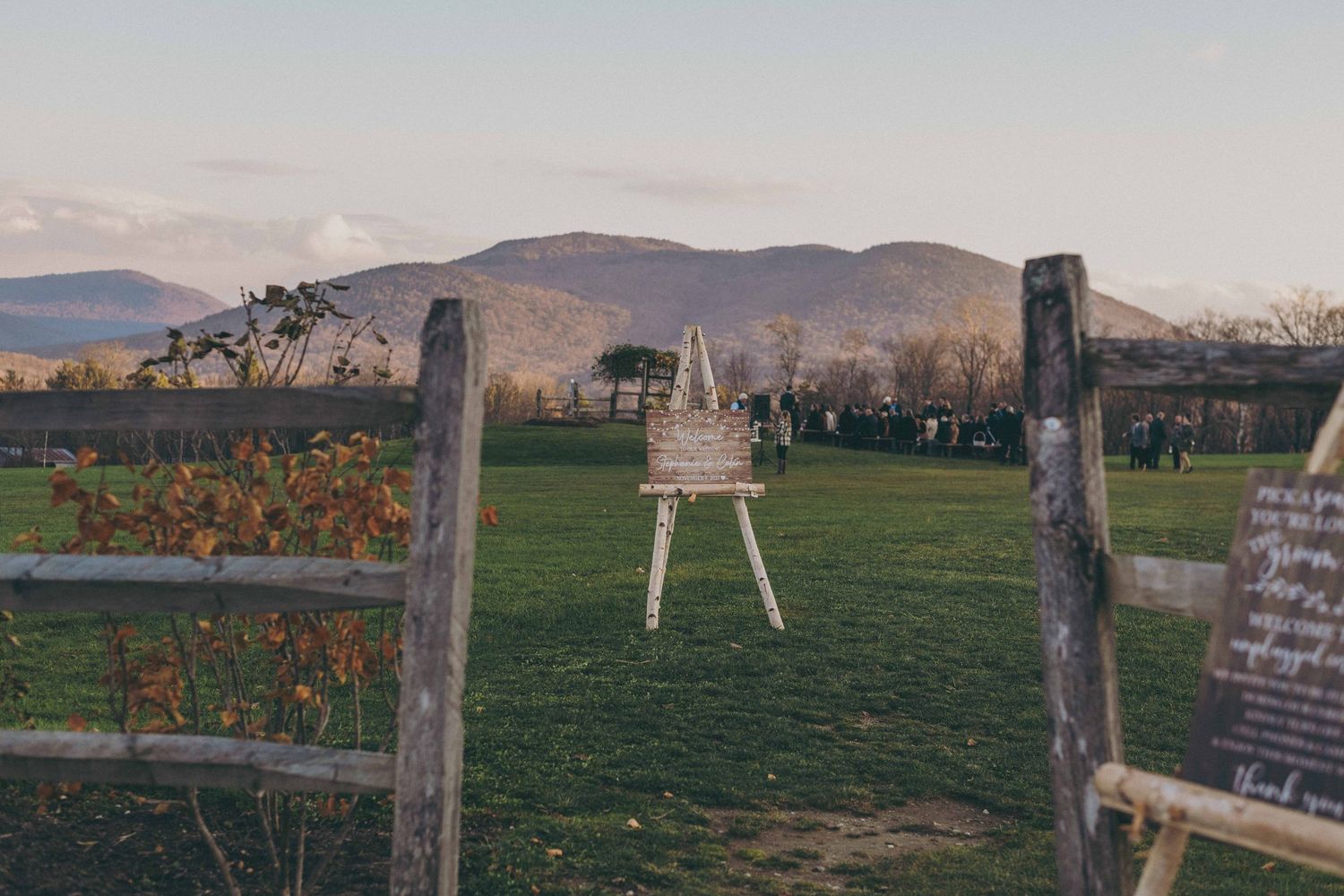 An outdoor wedding ceremony setup with wooden posts and a white arch against a mountain backdrop at sunset.