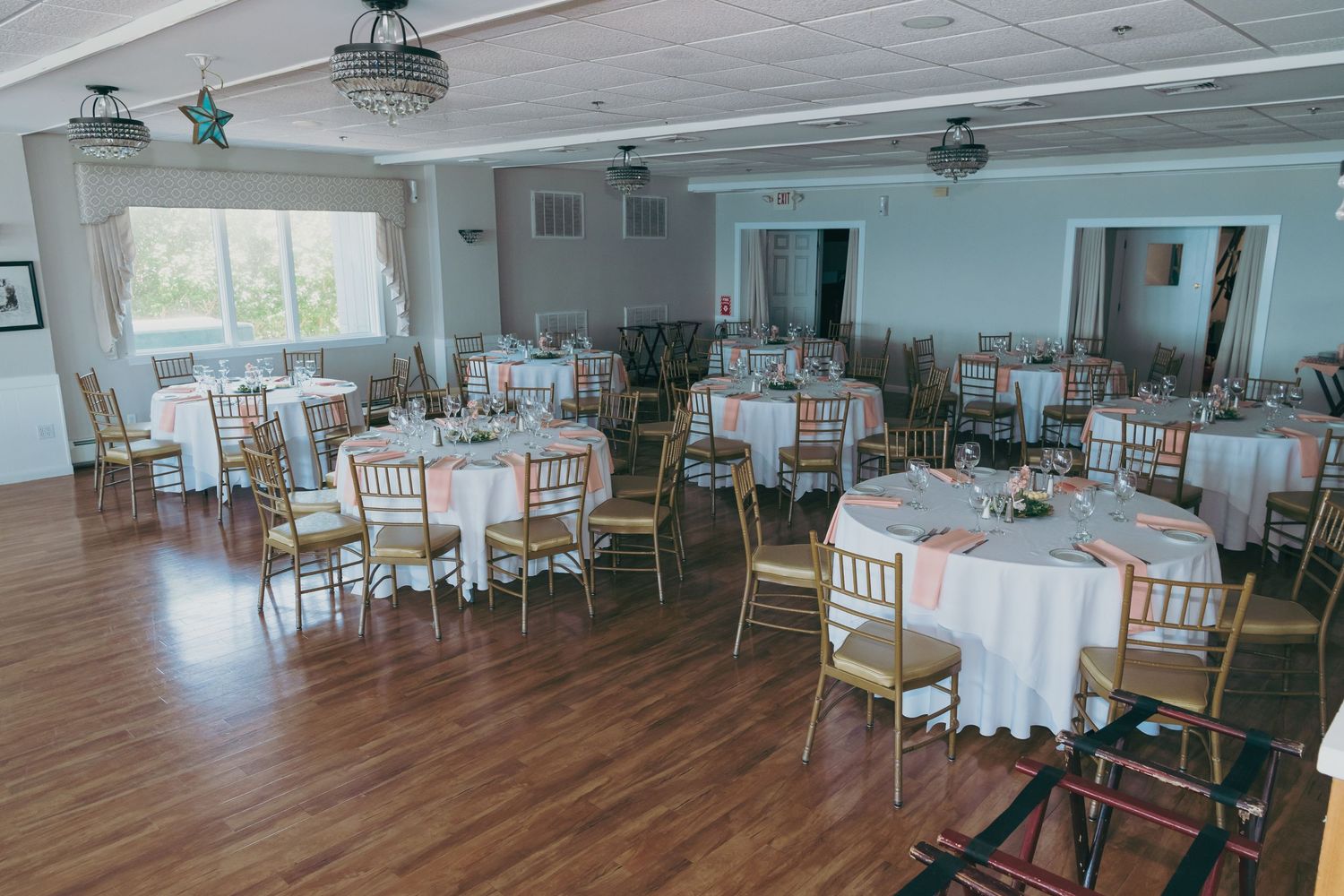 An elegant wedding reception venue with round tables, white linens, and gold chairs arranged in a bright banquet room.