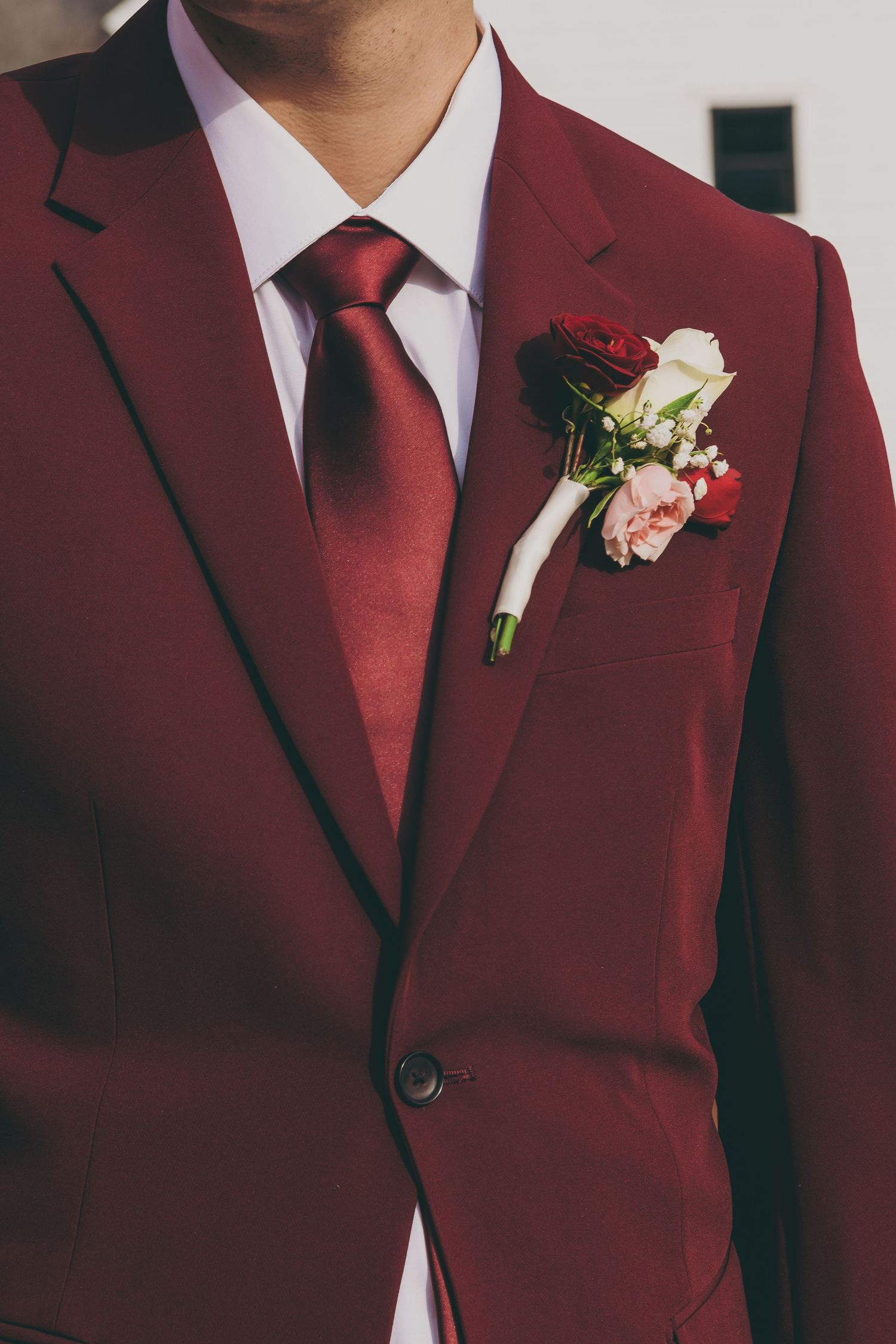 Wedding party members wearing burgundy suits with black lapels and white boutonnieres against a neutral background.