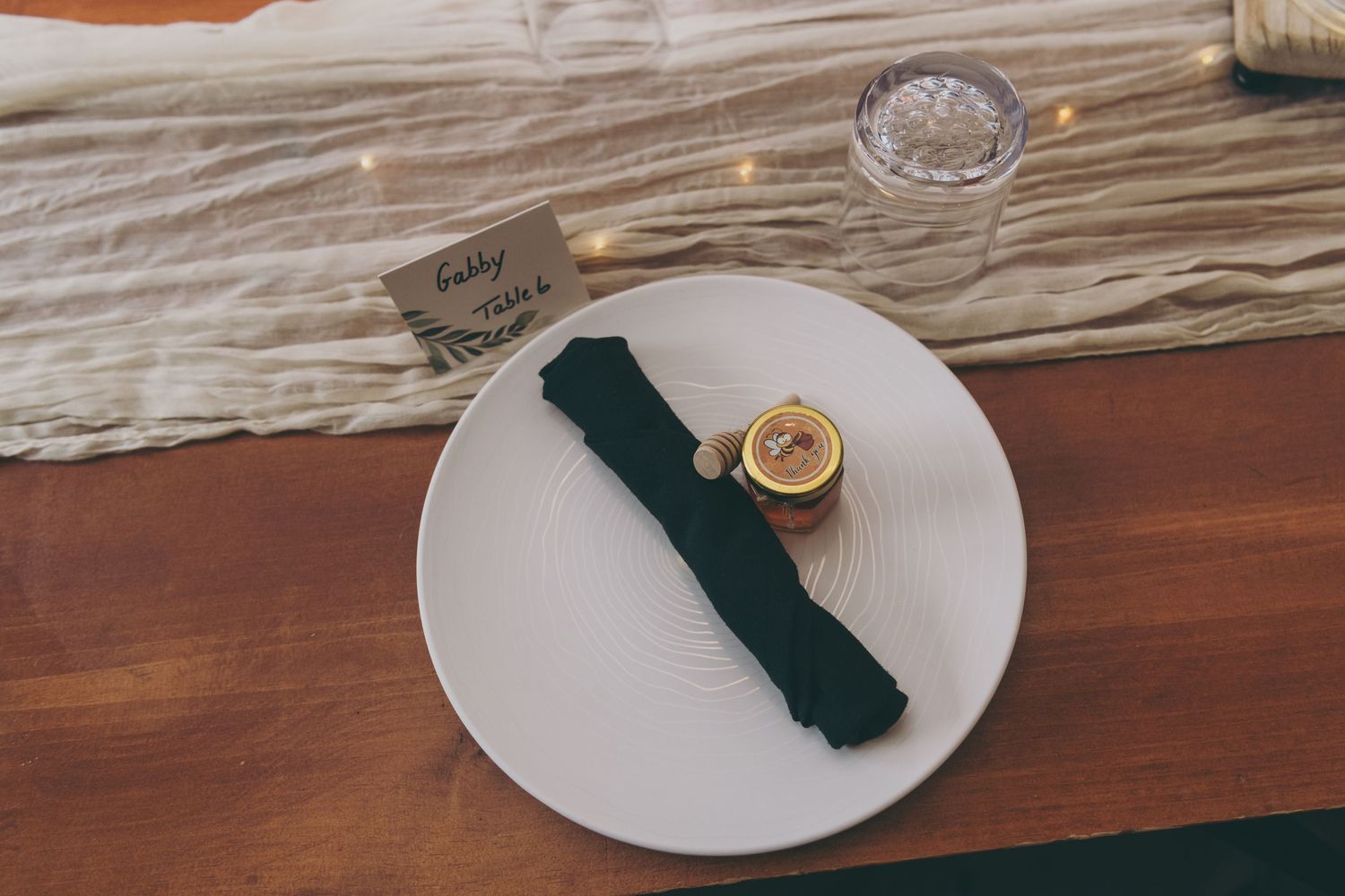 Place setting with green linen napkin and butter pat on white plate atop wooden table with rustic textured linen.