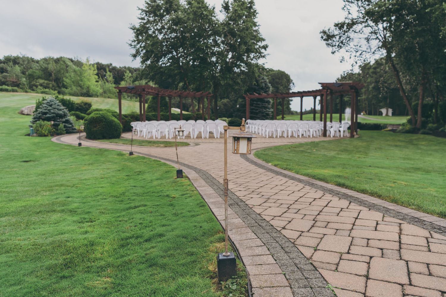 A curved stone walkway bordered by lush green grass winds through a scenic lakeside park landscape.