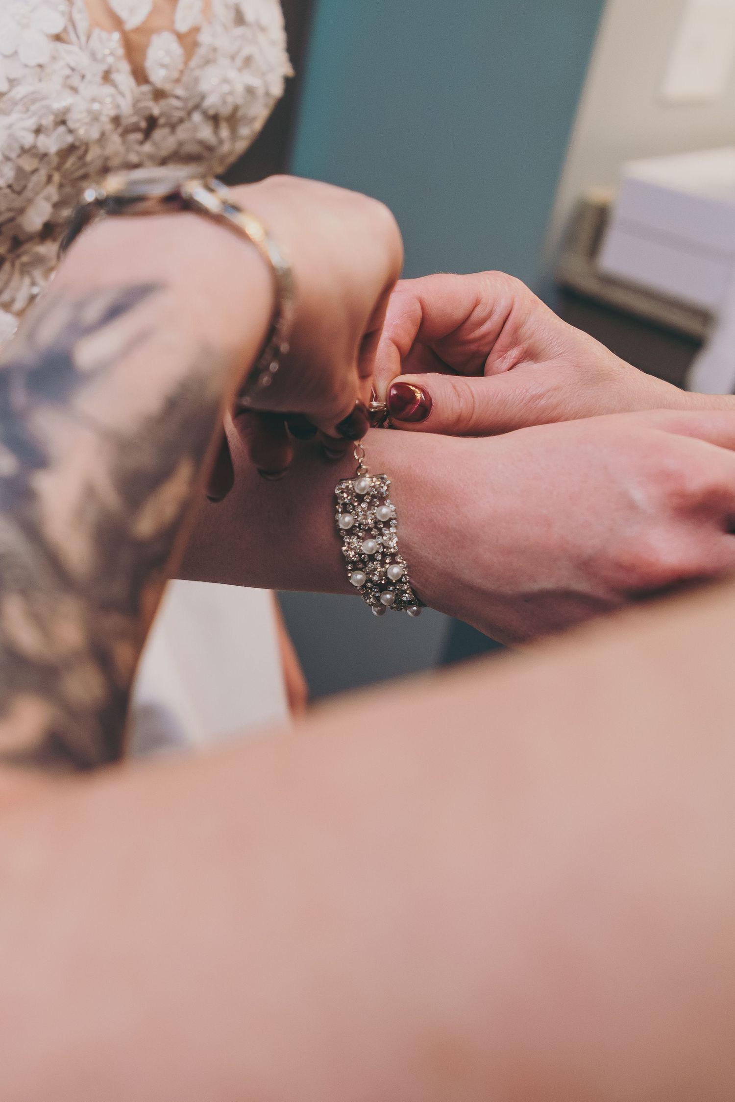 Hands putting on an ornate crystal bracelet with sparkly rhinestones against a teal background.