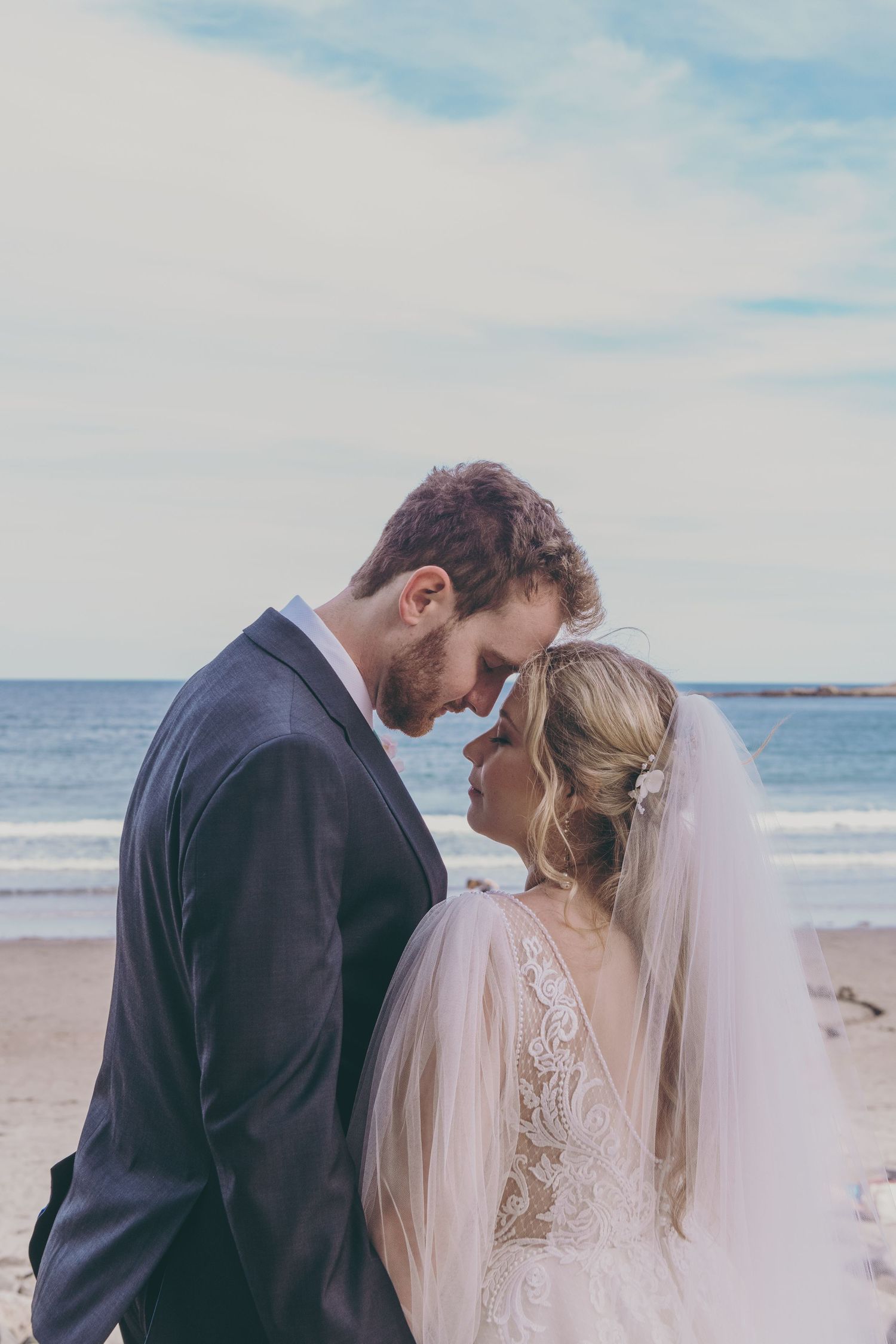 A romantic beach wedding scene with a couple sharing an intimate moment by the ocean in formal attire.