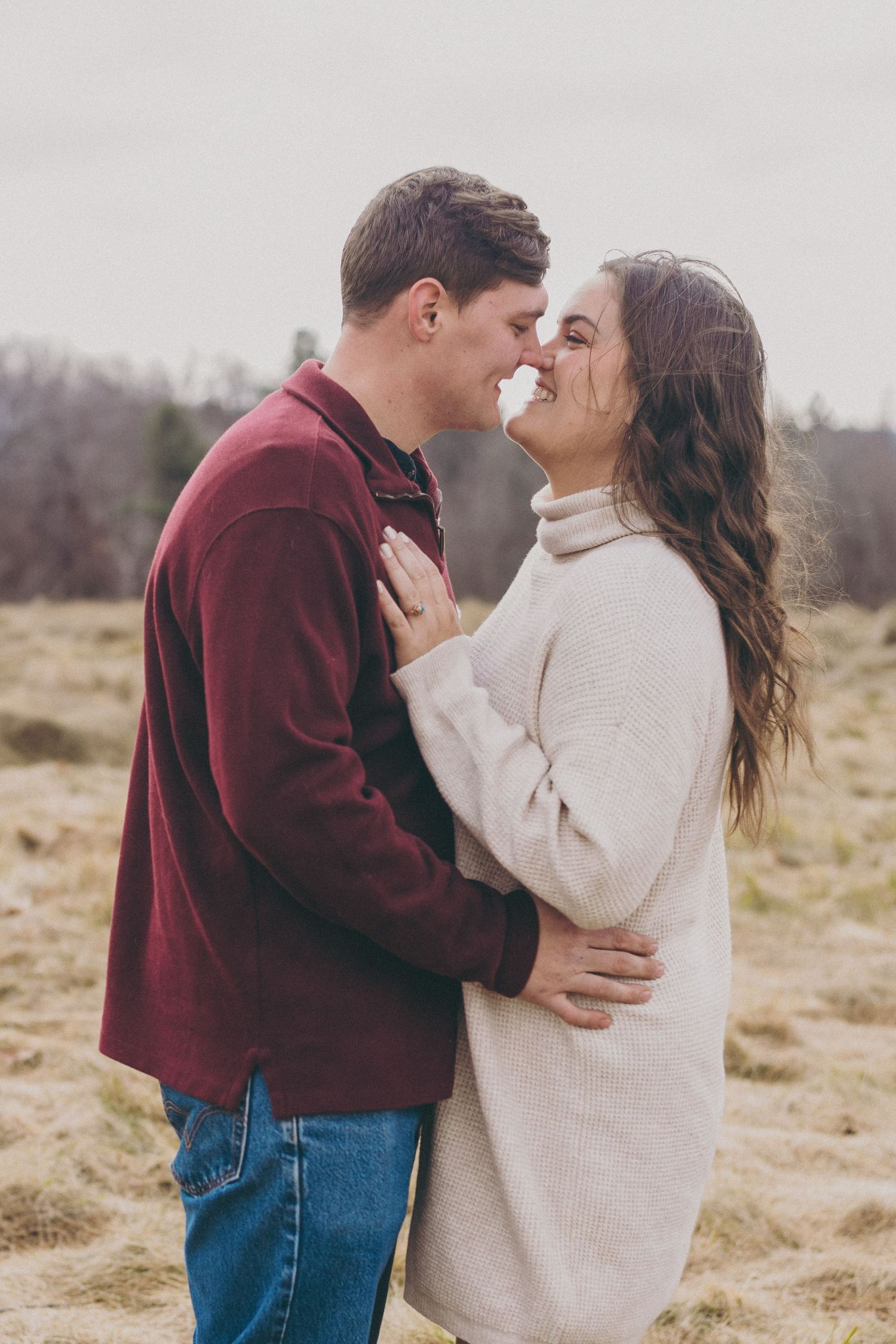 Romantic couple in burgundy and cream sweaters embracing in a winter field.