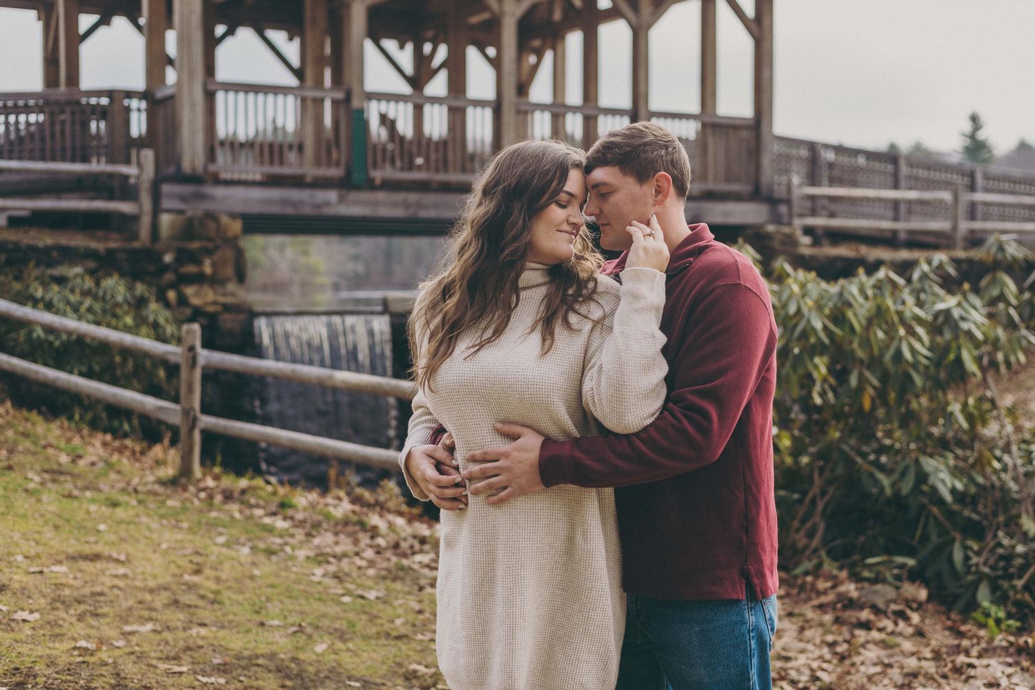 Couple sharing romantic moments near a rustic wooden bridge and stone wall.