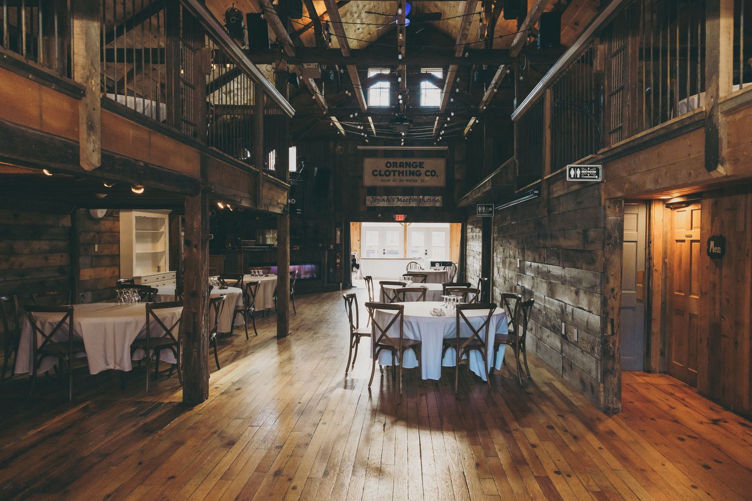 Rustic barn venue interior with wooden beams and tables set for an event featuring hardwood floors and natural lighting.