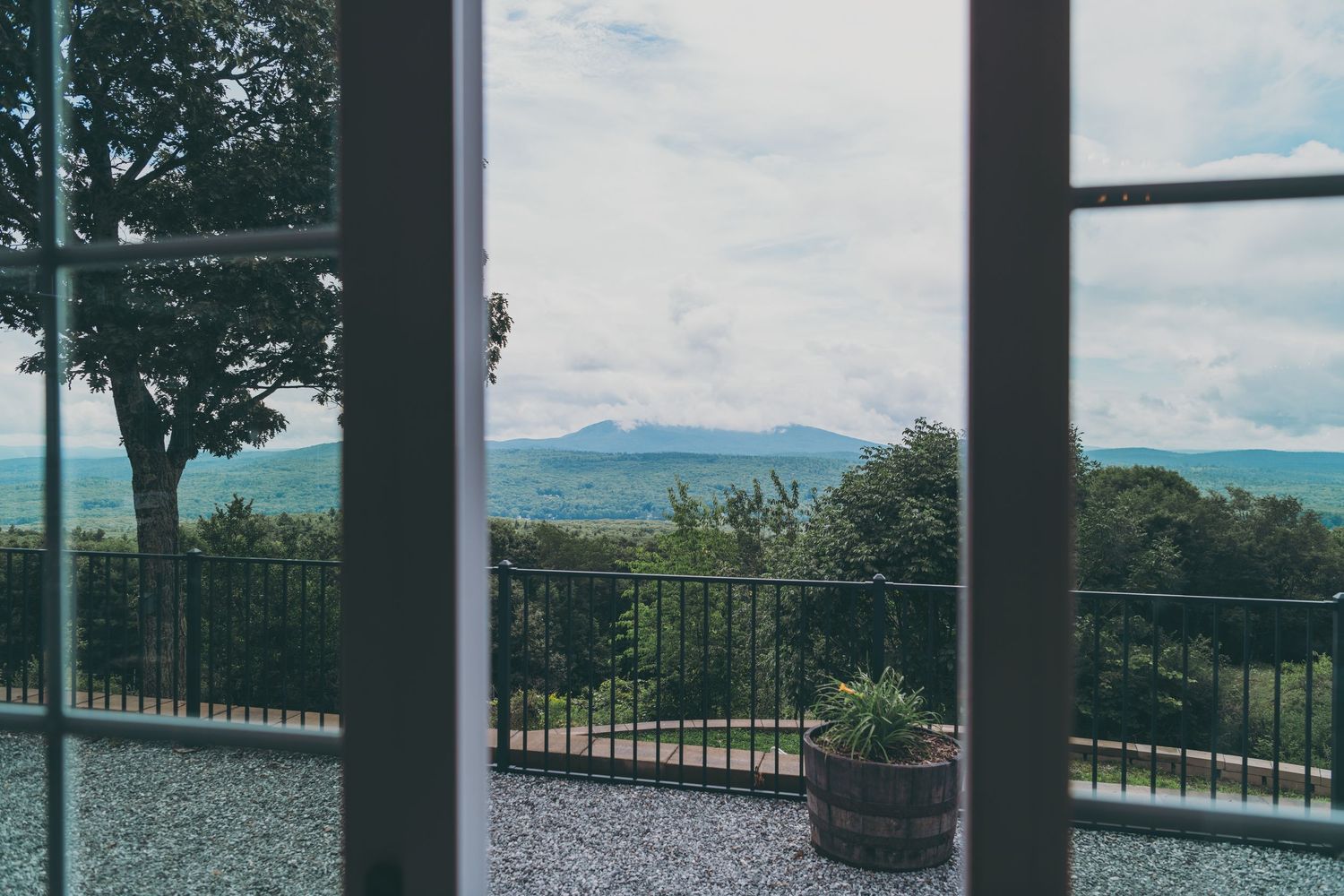Scenic mountain landscape viewed through a window frame with metal railing and potted plants on a patio.