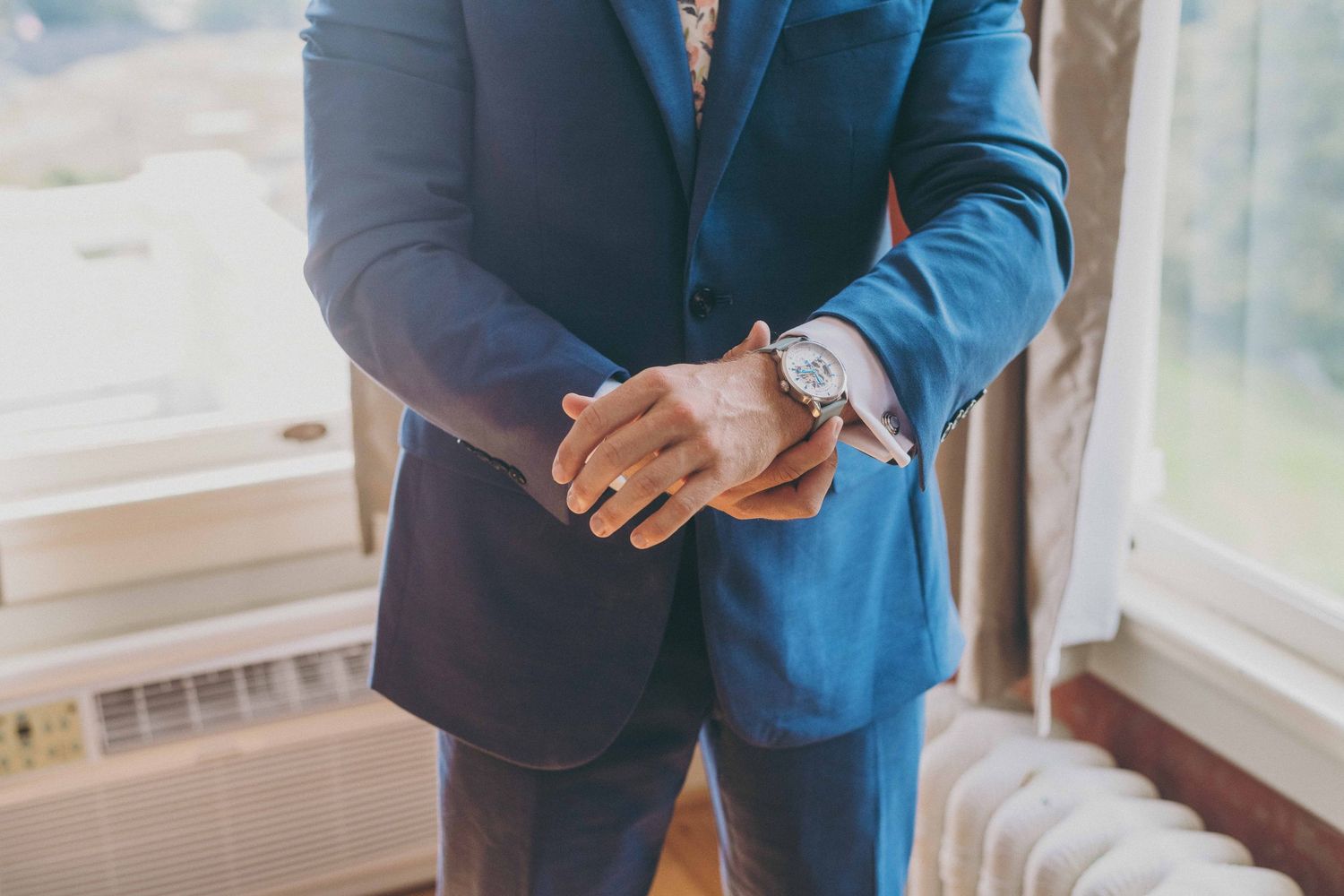 Close-up view of someone wearing a blue suit and checking their wristwatch near a window.