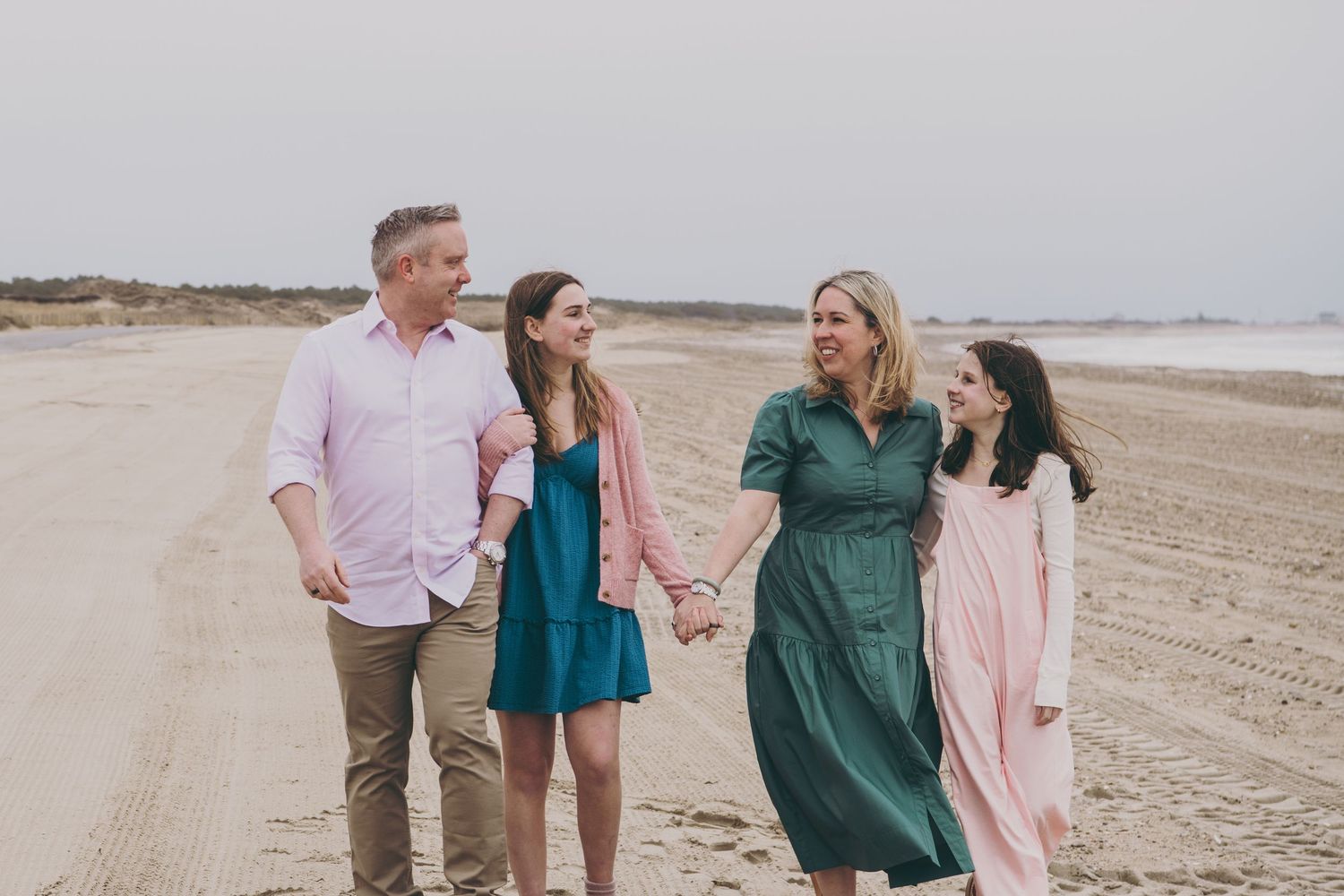 A group of people walking together and smiling on a sandy beach with mountains visible in the distance.
