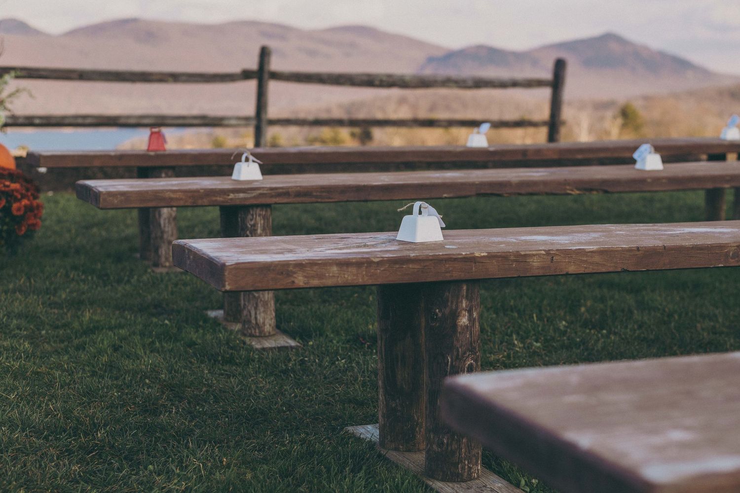 Rustic wooden benches with backrests arranged in rows face mountains in a scenic outdoor setting.