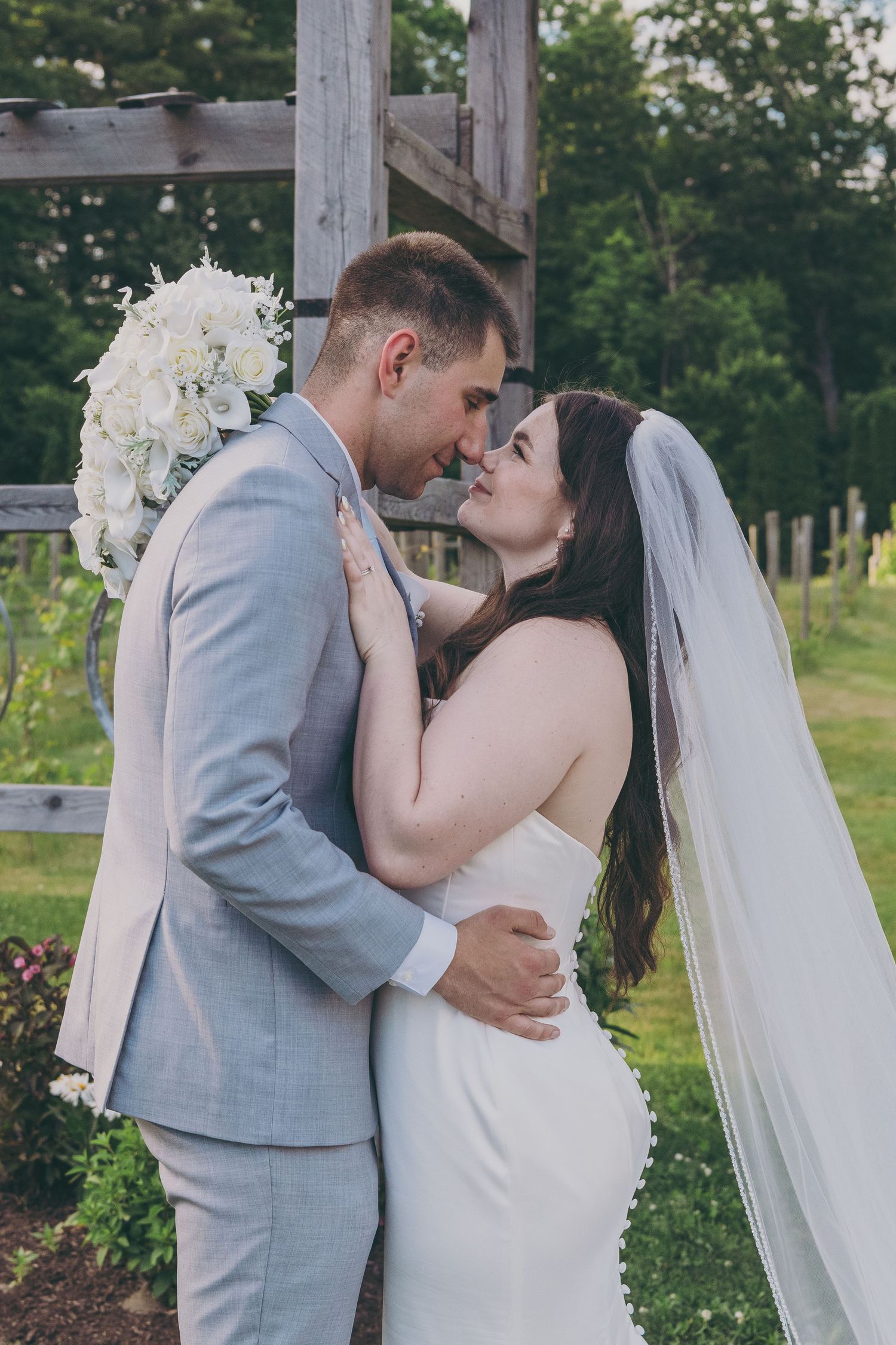 A romantic outdoor wedding moment at a vineyard with white floral decorations and rustic wooden backdrop.
