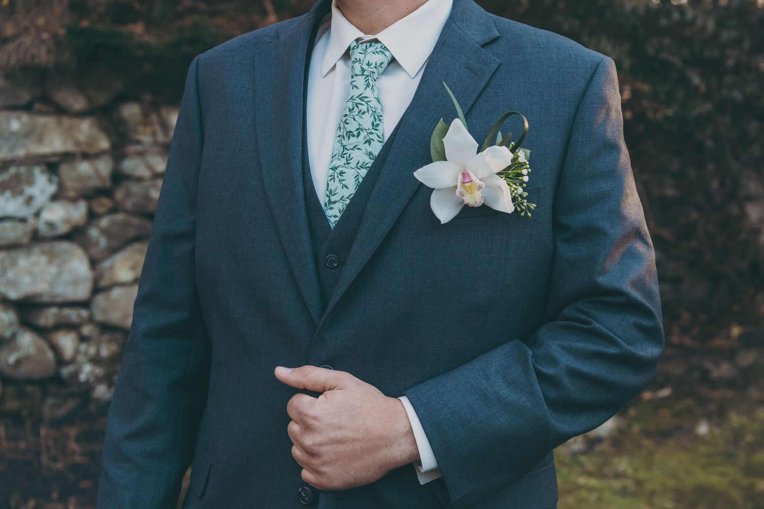 Close up of groom's suit jacket with floral boutonniere and seafoam green patterned tie.