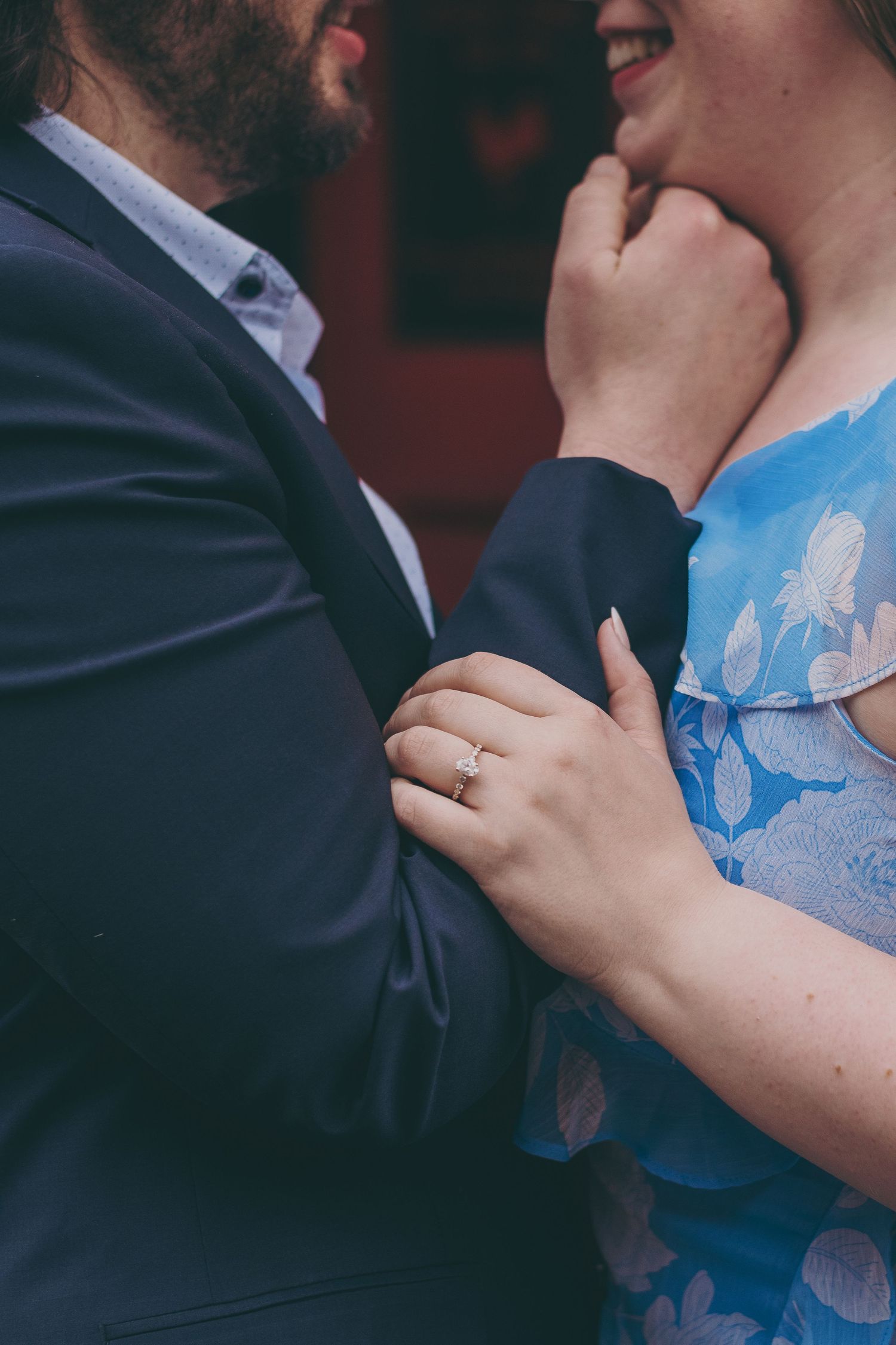 Close up detail of two people embracing, showing a blue floral dress and dark suit fabric.