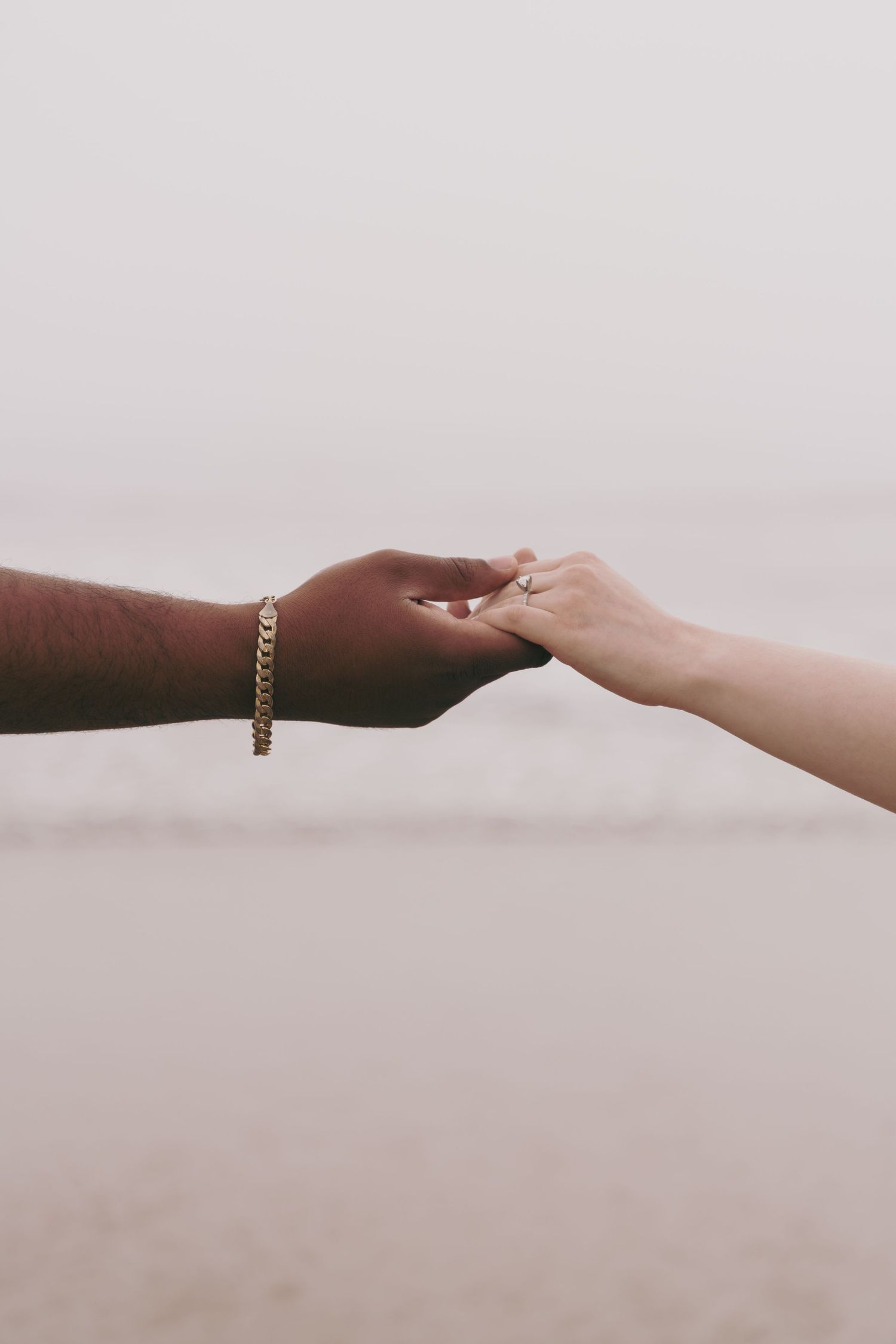Two hands of different skin tones gently touch fingertips against a light background, one wearing a gold chain bracelet.