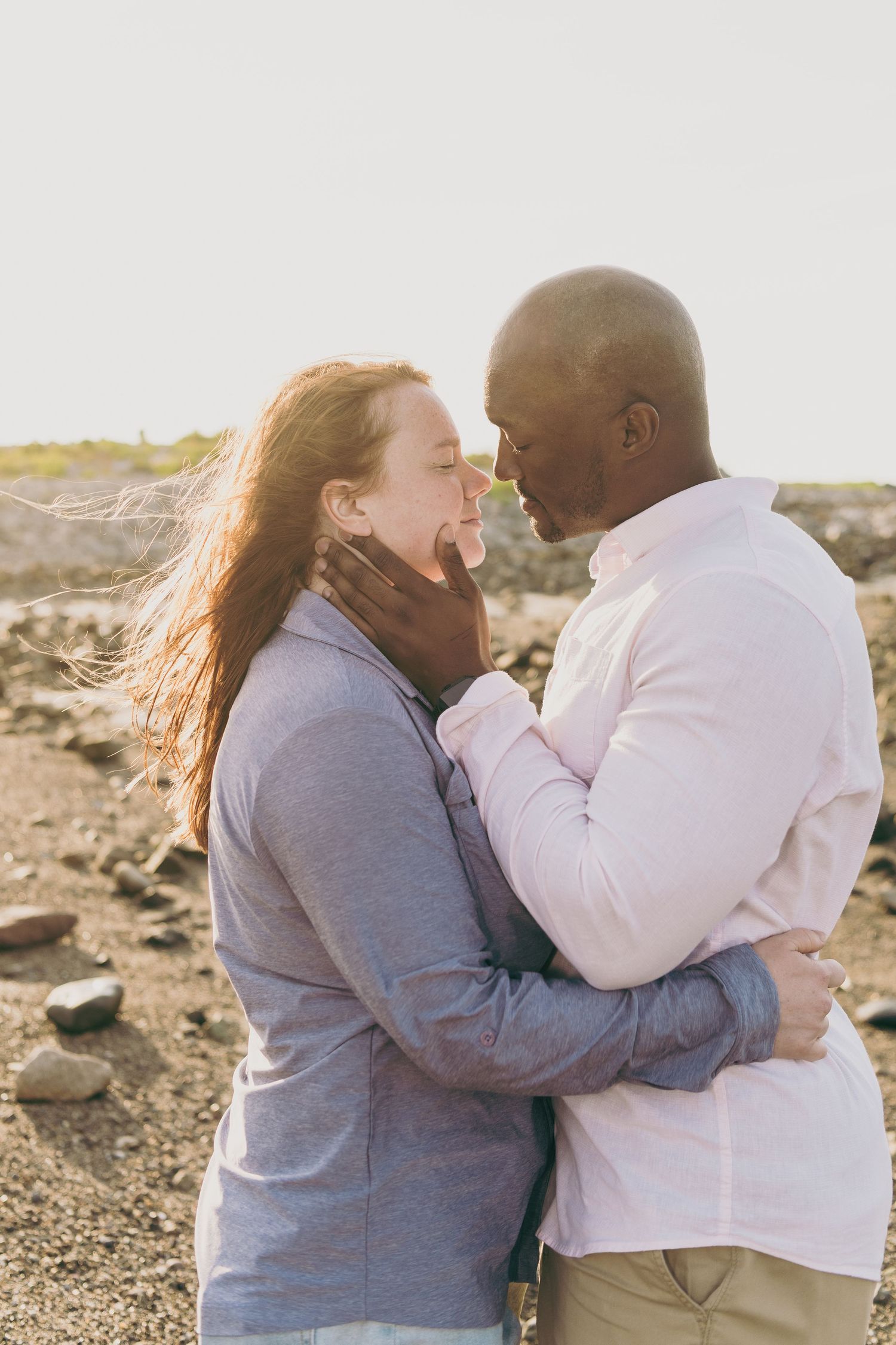 Joyful couple embraces and laughs together during a sunset photoshoot on rocky terrain.