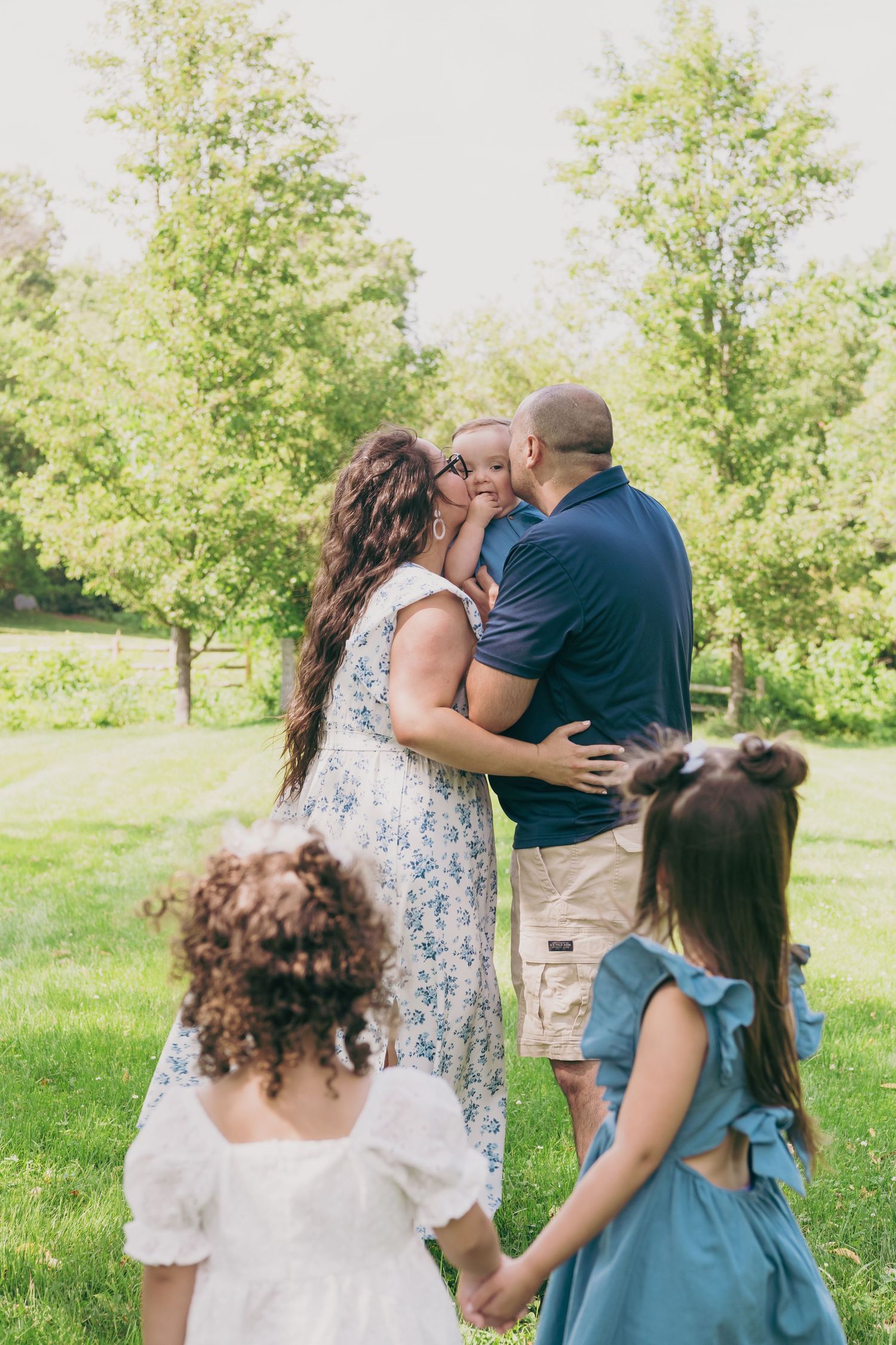 A tender moment shared outdoors on a sunny day in a grassy park with trees in the background.