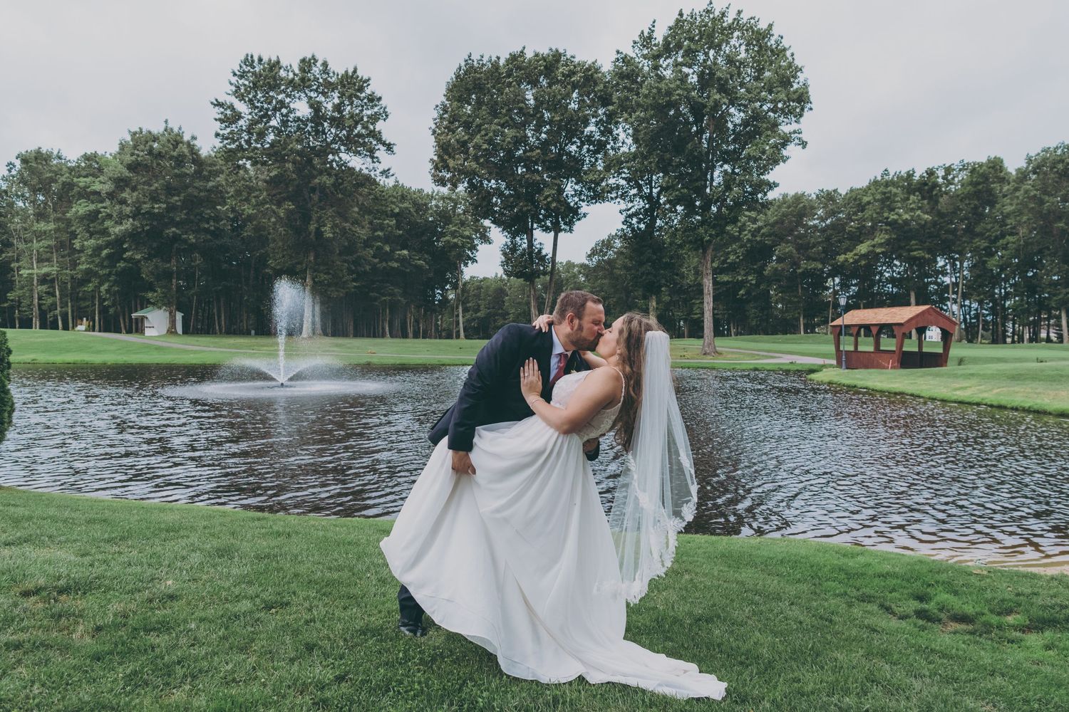 A romantic moment captured by a pond with a fountain at a golf course wedding venue.
