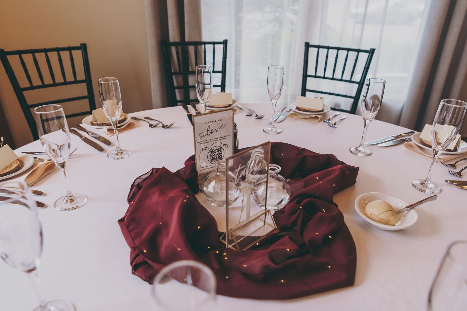 An elegant wedding table setting with dark red linens and a centerpiece featuring a white lantern on a round table.