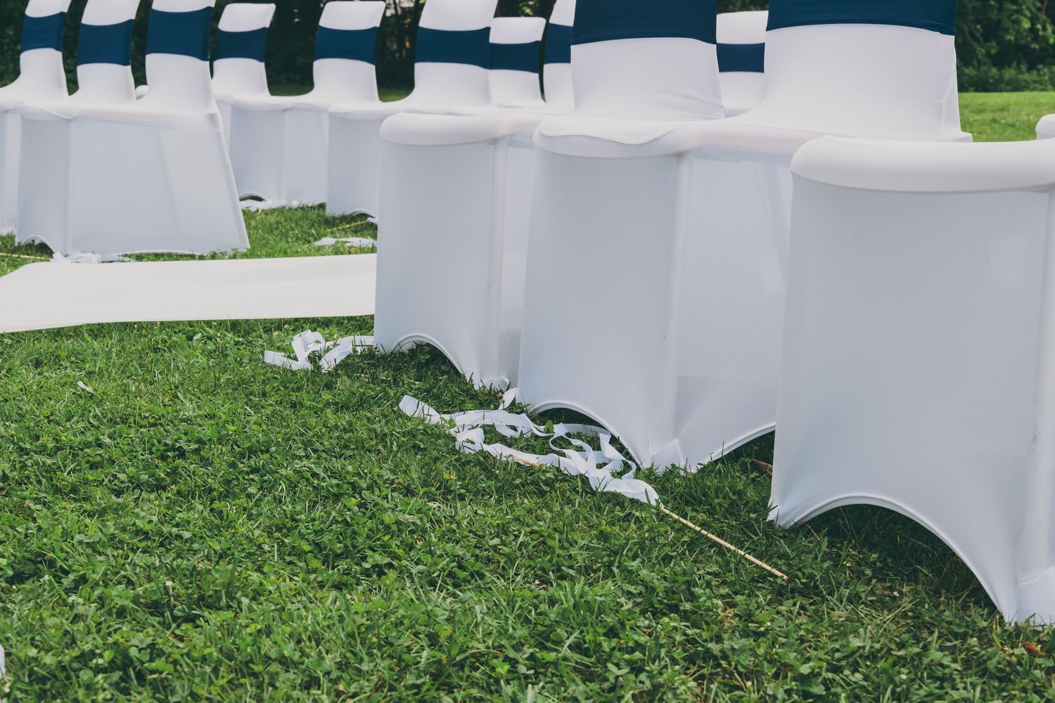 White folding chairs with spandex covers set up on green grass for an outdoor wedding ceremony.