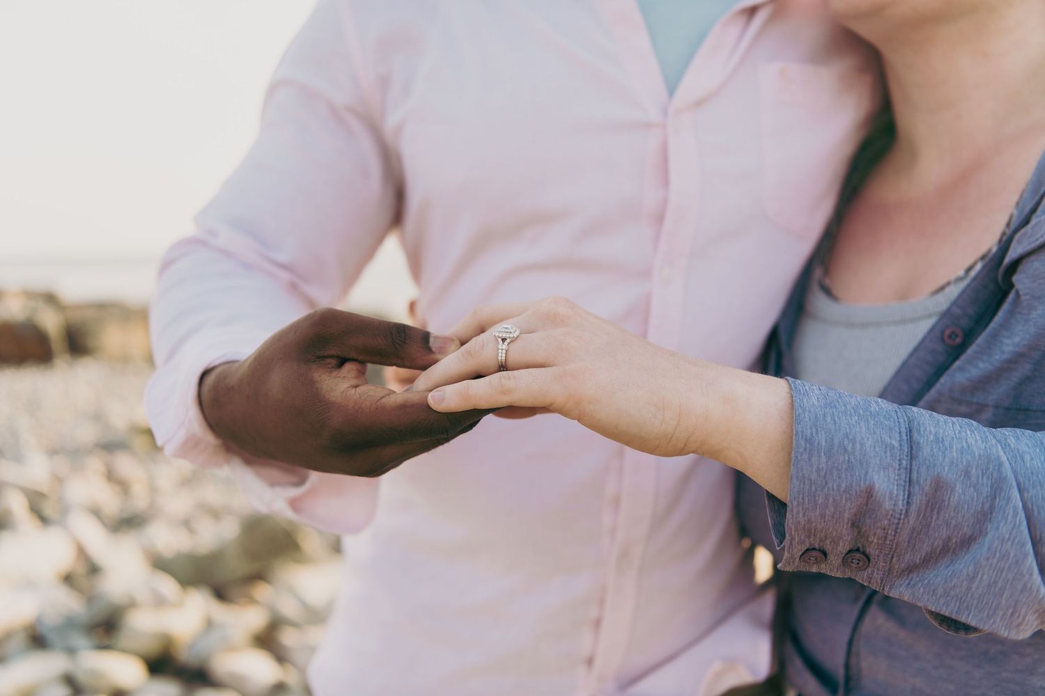 Two hands exchange an engagement ring during a romantic seaside proposal moment.