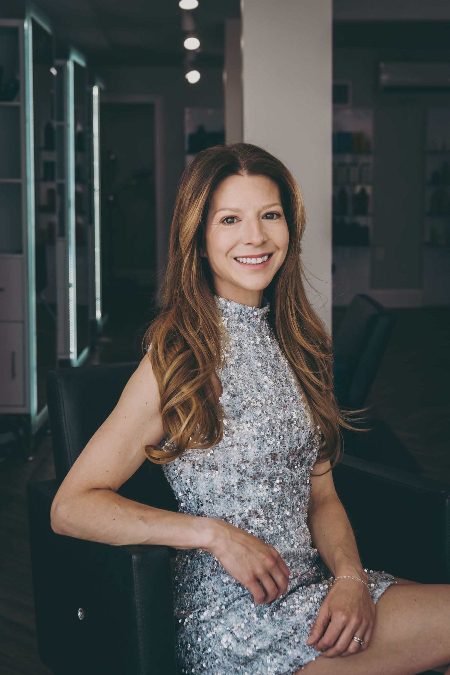 Woman in sparkling silver dress poses elegantly in modern studio setting.