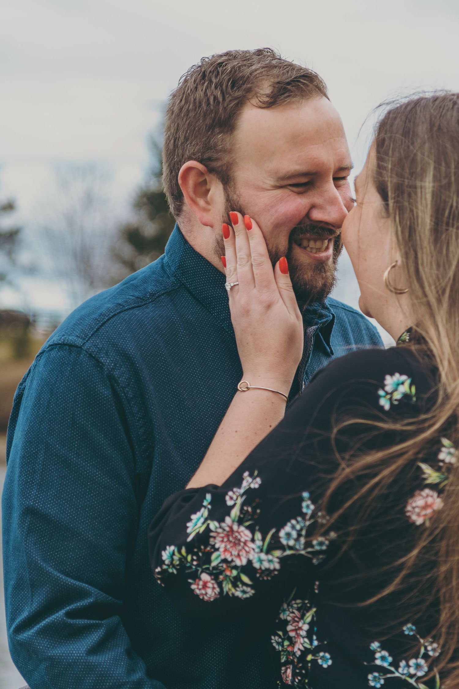 A tender moment captured between a couple in casual attire against a cloudy backdrop.