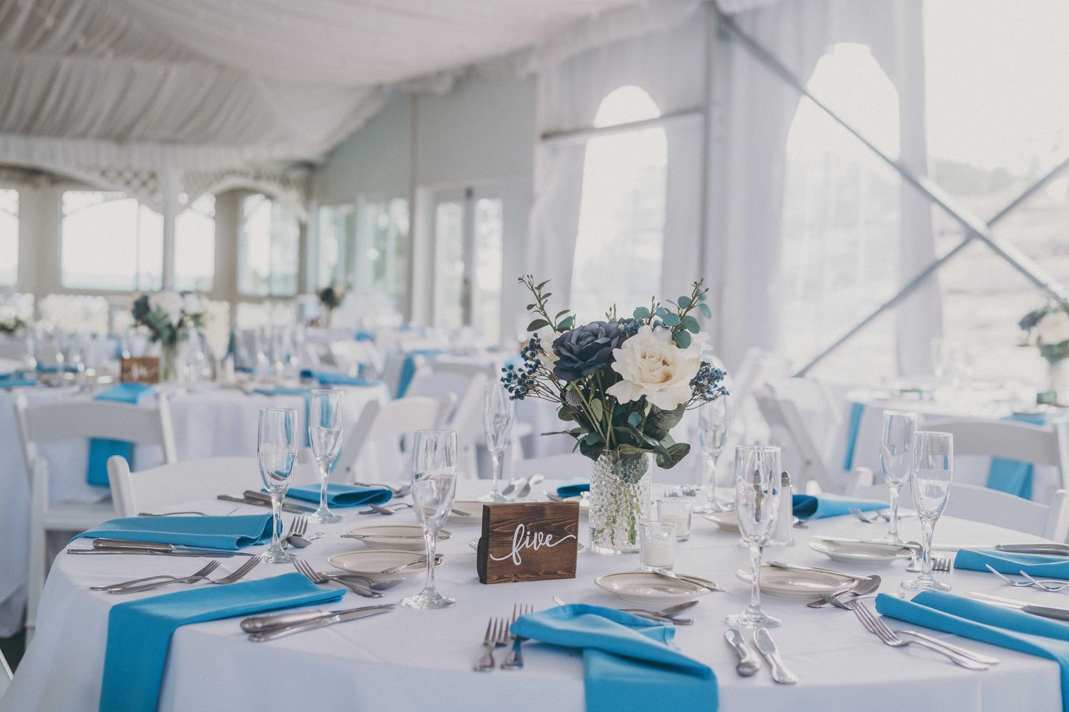 Wedding reception tables decorated in white and turquoise with elegant floral centerpieces and place settings.