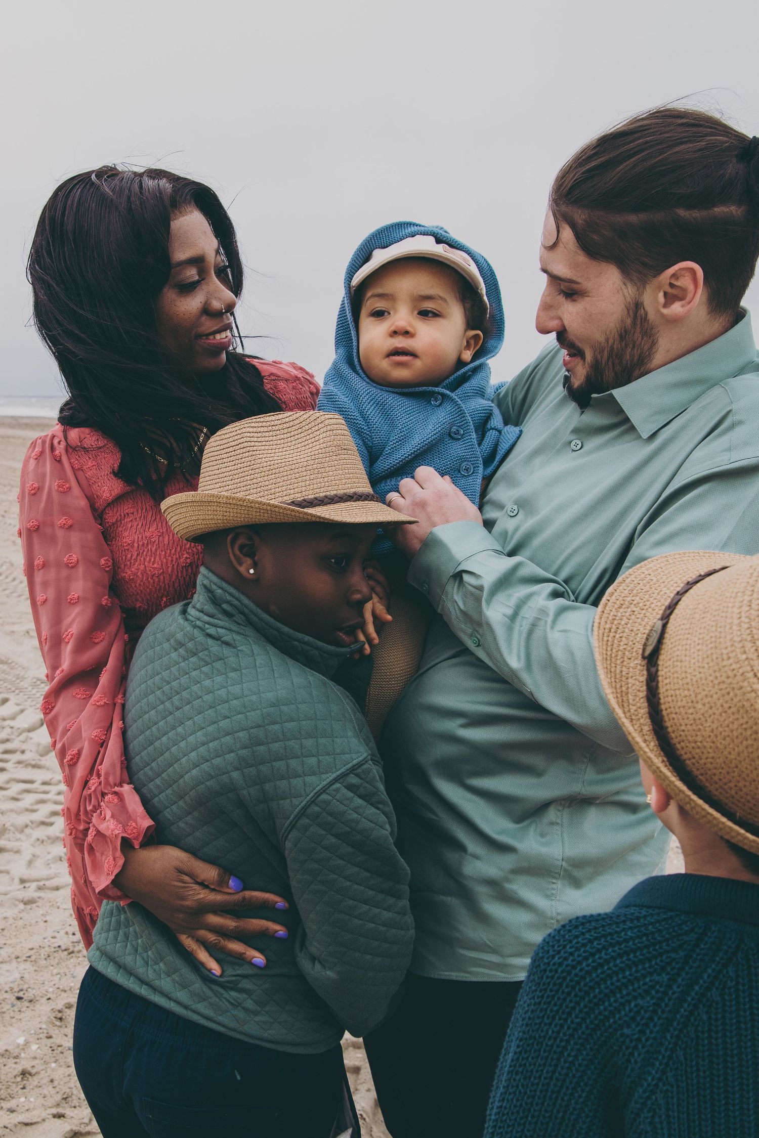 Family wearing casual clothing embraces tenderly while enjoying time together at beach during sunset.