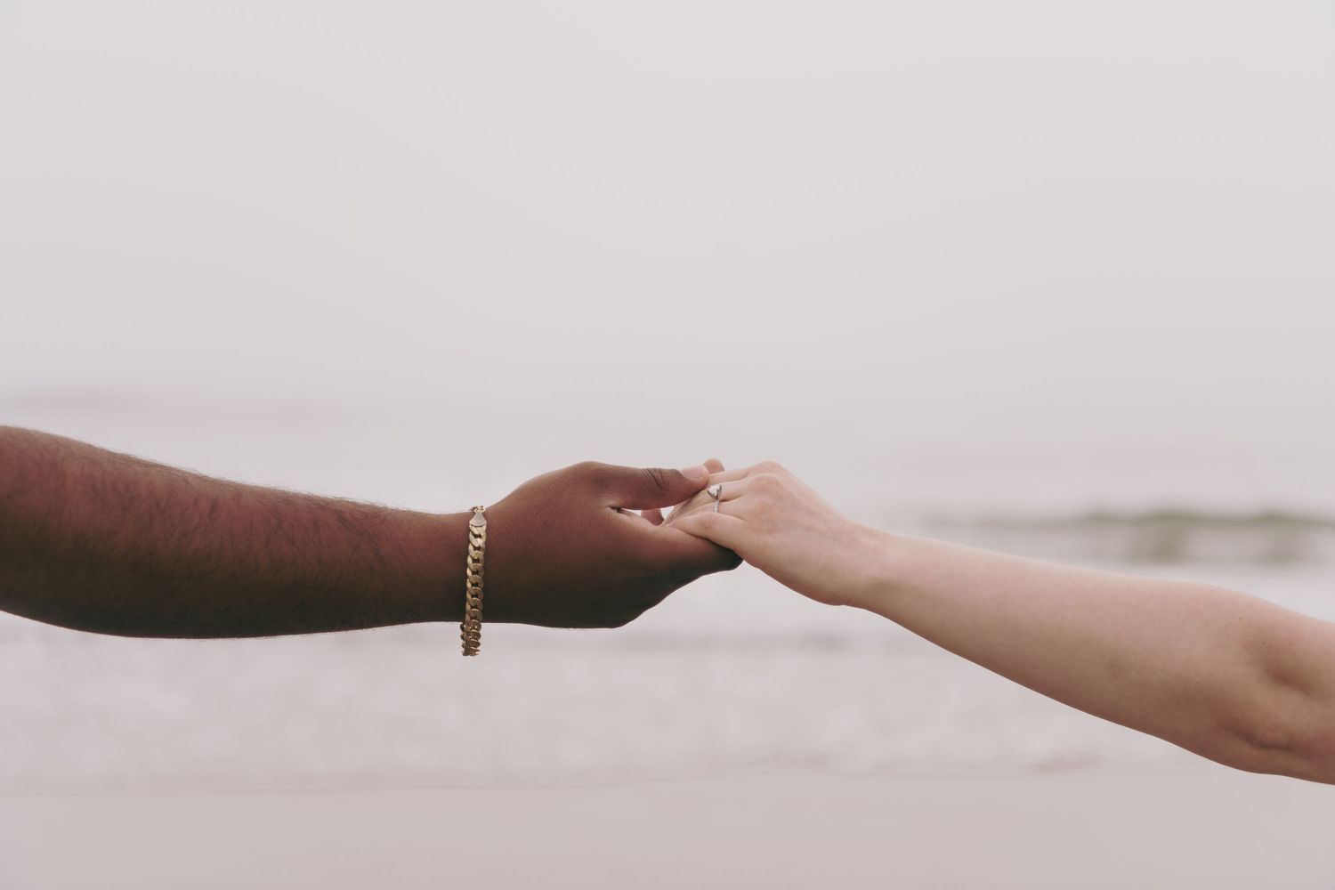 Two hands of different skin tones reaching out to touch each other against a soft neutral background.