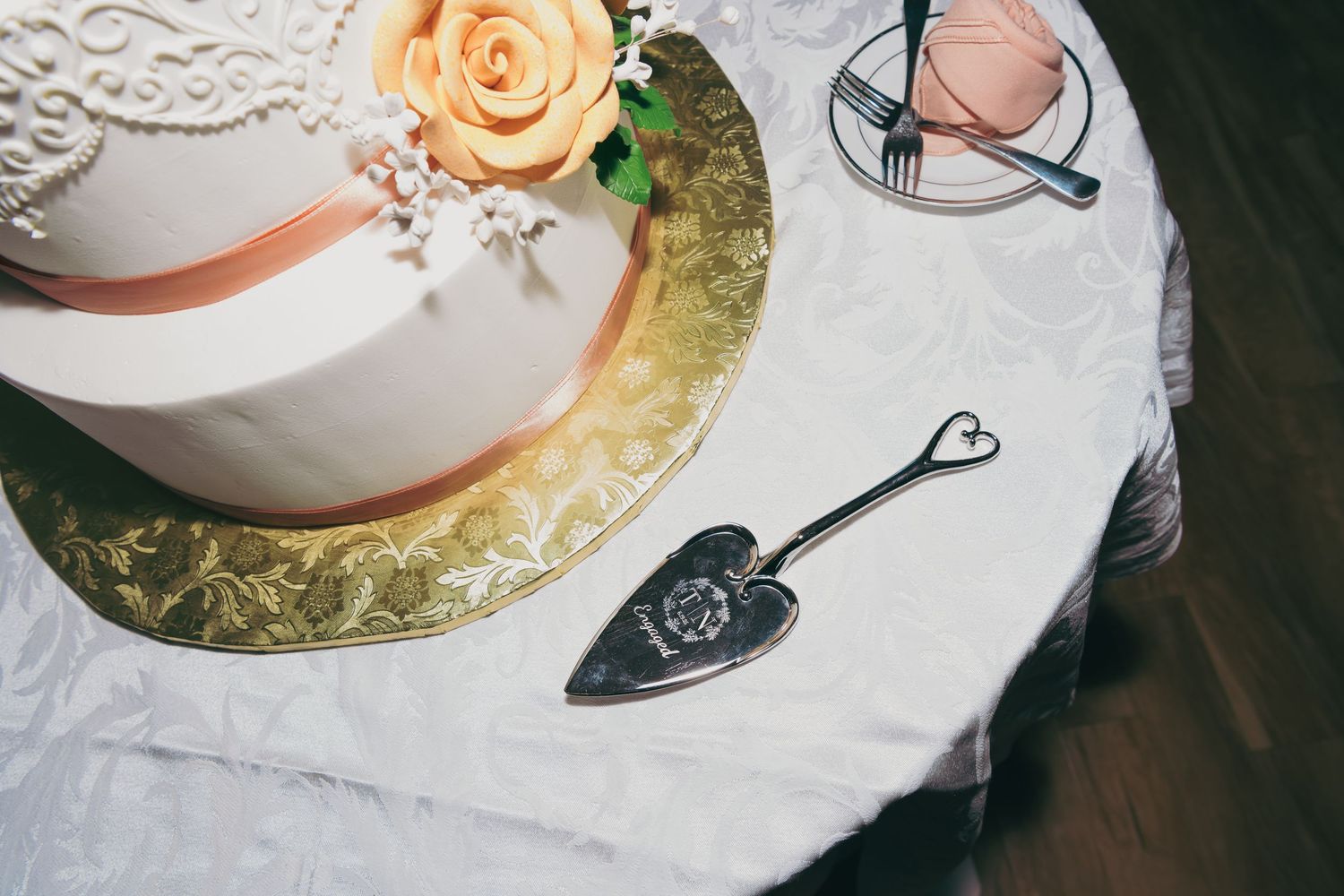 Vintage table setting with delicate peach rose, white dishes, and decorative silver serving utensils on lace tablecloth.