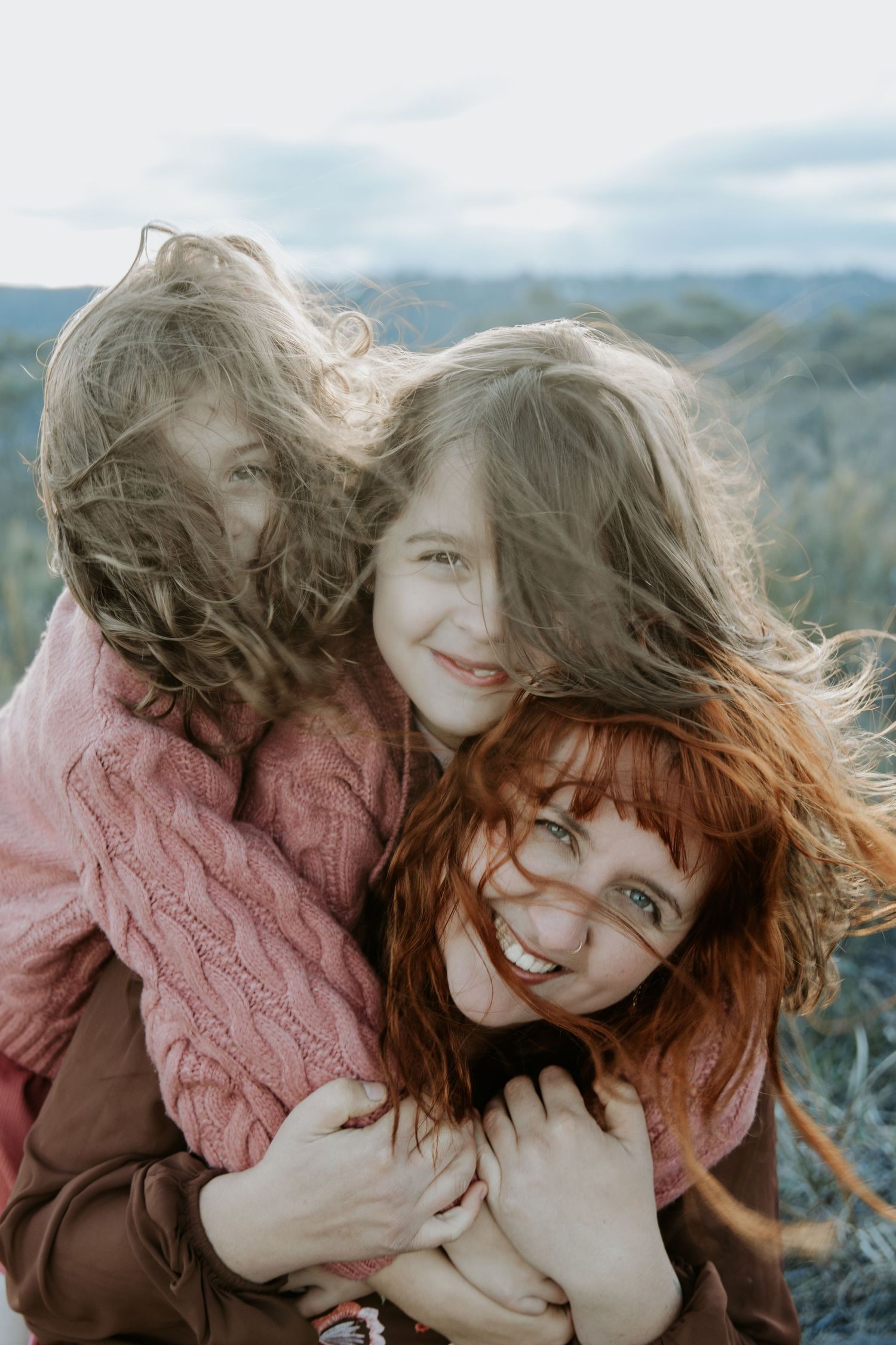 A mother with her two daughters embracing on a windy day in the blue mountains