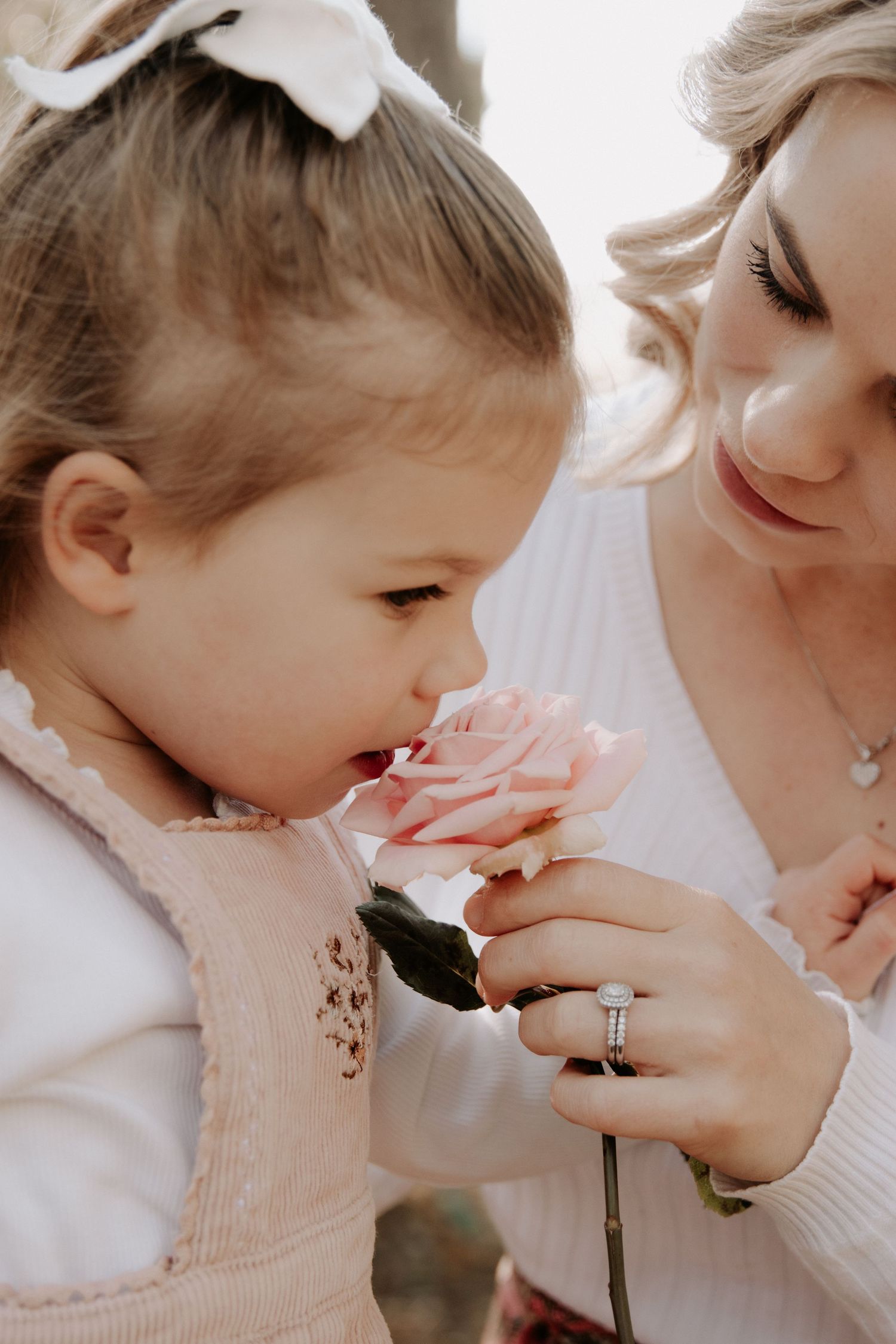A mother letting her daughter smell a large pink rose